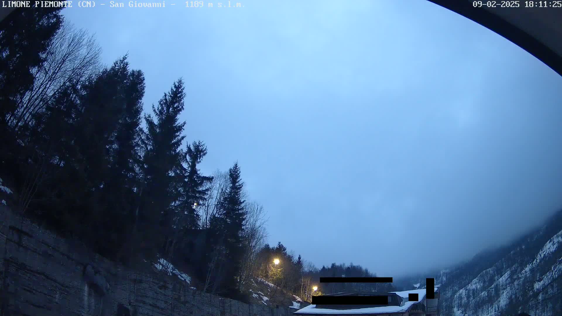 A twilight view of a mountain road lined with evergreens, with a light fog settling in the valley below.