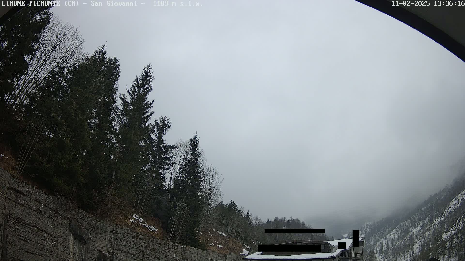 A foggy, overcast day reveals a rocky hillside covered in evergreens and a partially visible building.