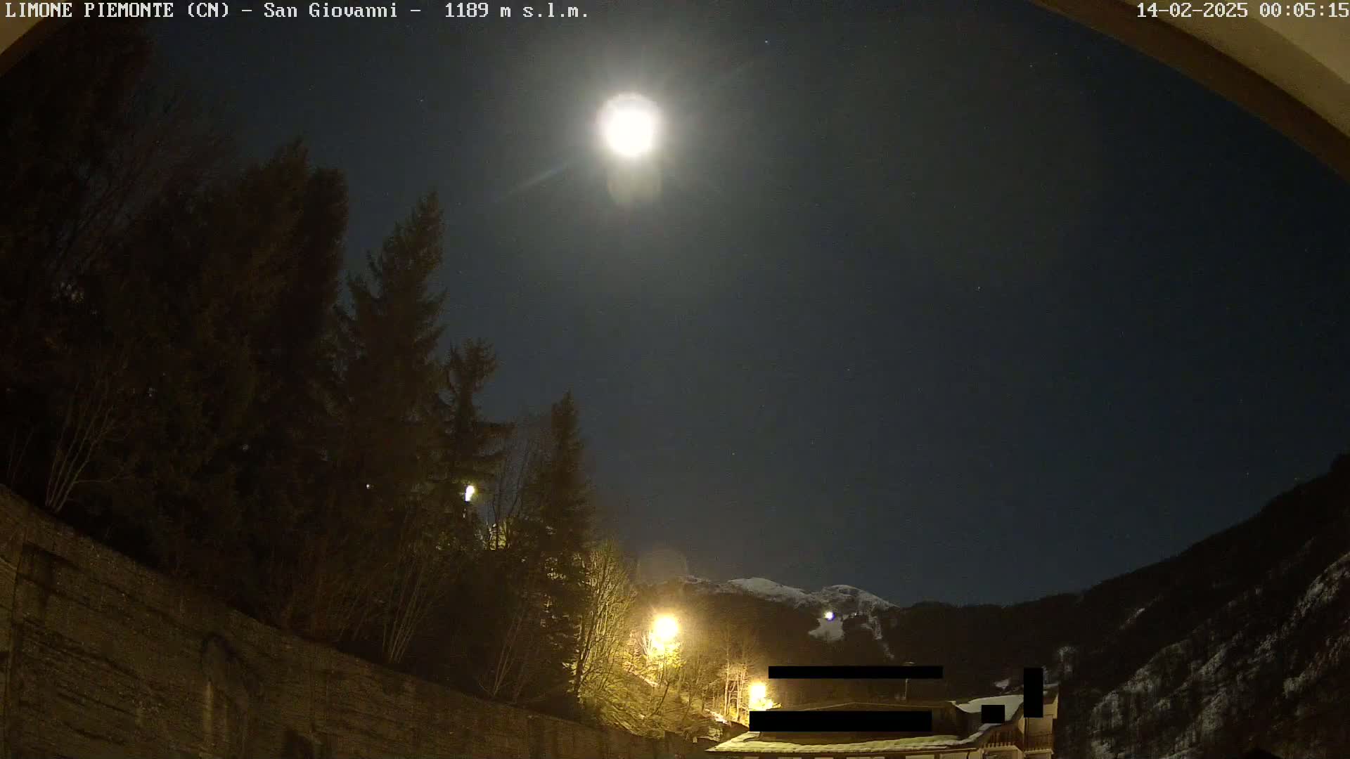 A bright moon illuminates a nighttime scene of dark trees, a stone wall, and snow-capped mountains in the distance.