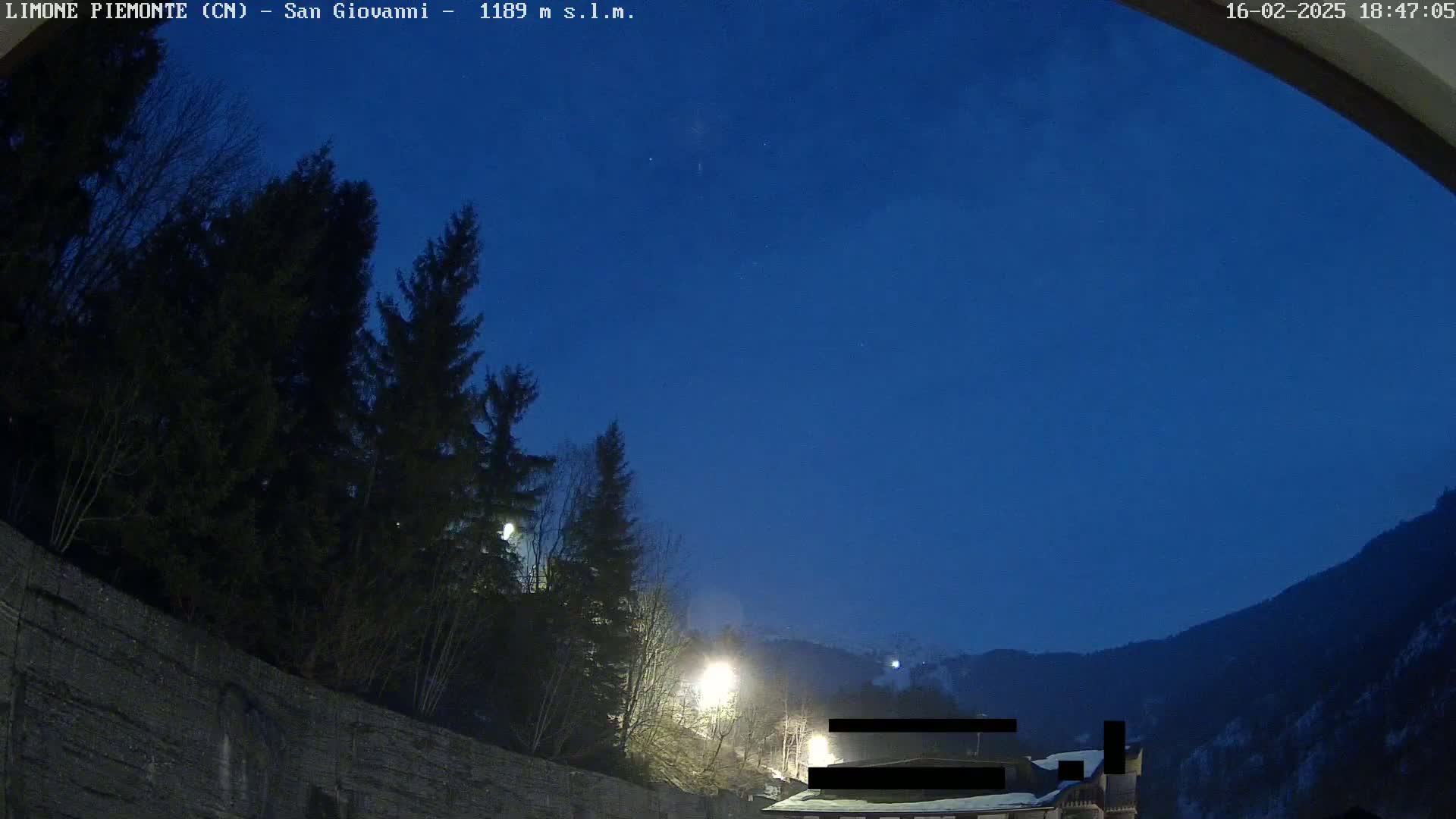 A nighttime view of dark evergreen trees and a mountainside under a clear, dark blue sky, illuminated by several streetlights.