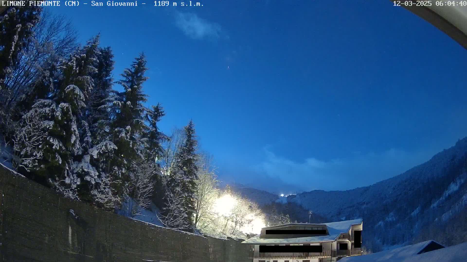 Snow-covered trees and a building are visible under a twilight blue sky, with a mountain range in the background.