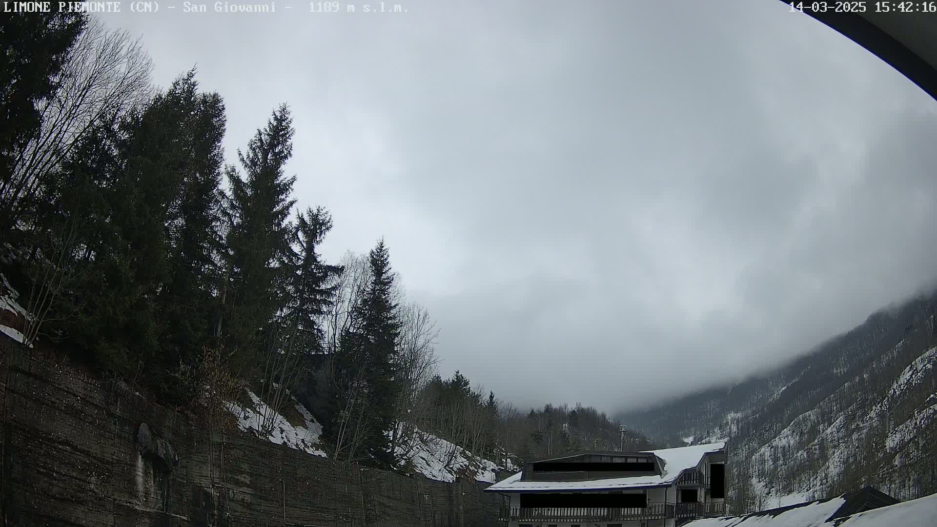 A building sits below a snow-covered mountainside under an overcast sky.