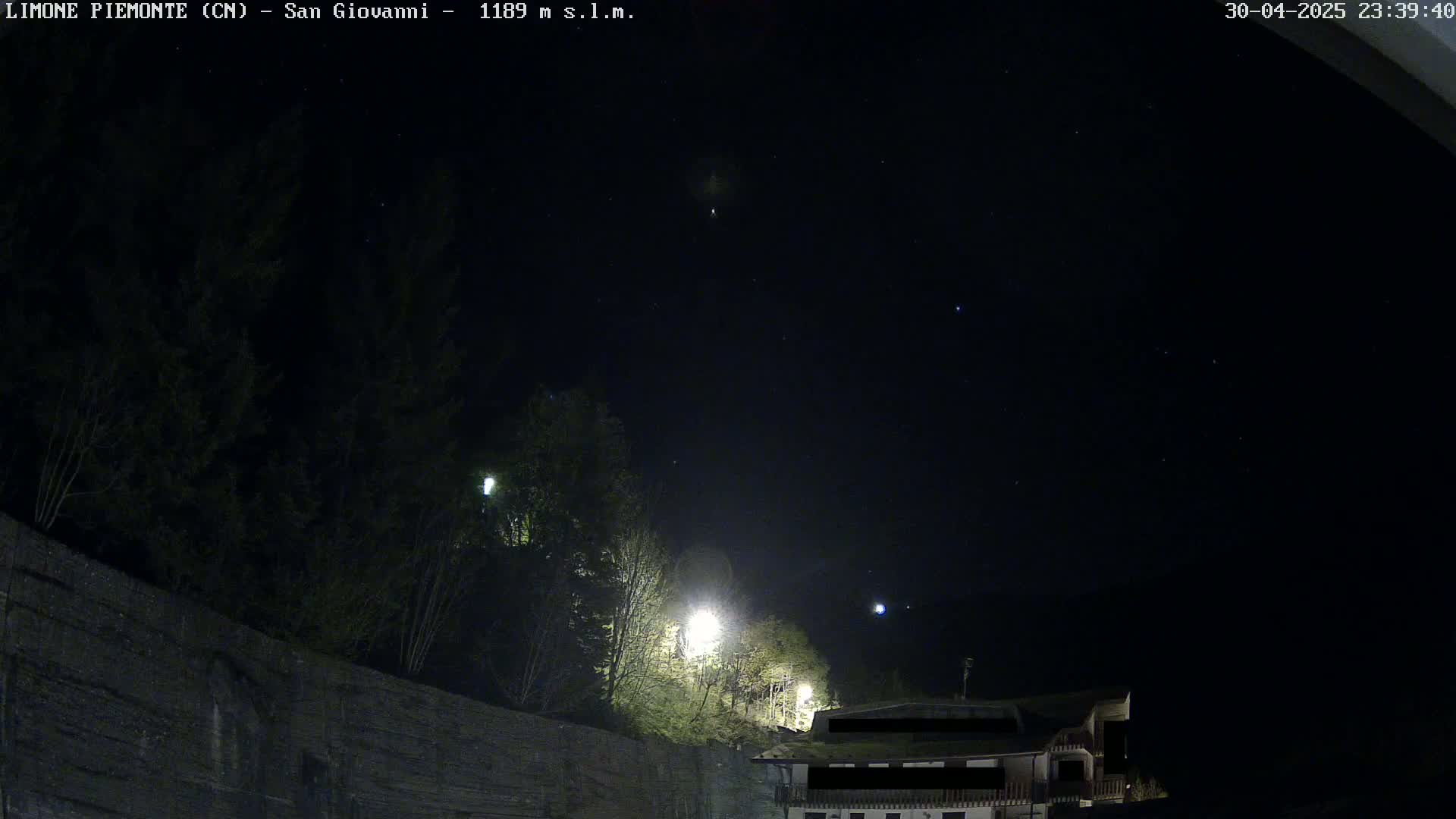 A nighttime view of a stone wall, trees, and a building under a clear, starlit sky.