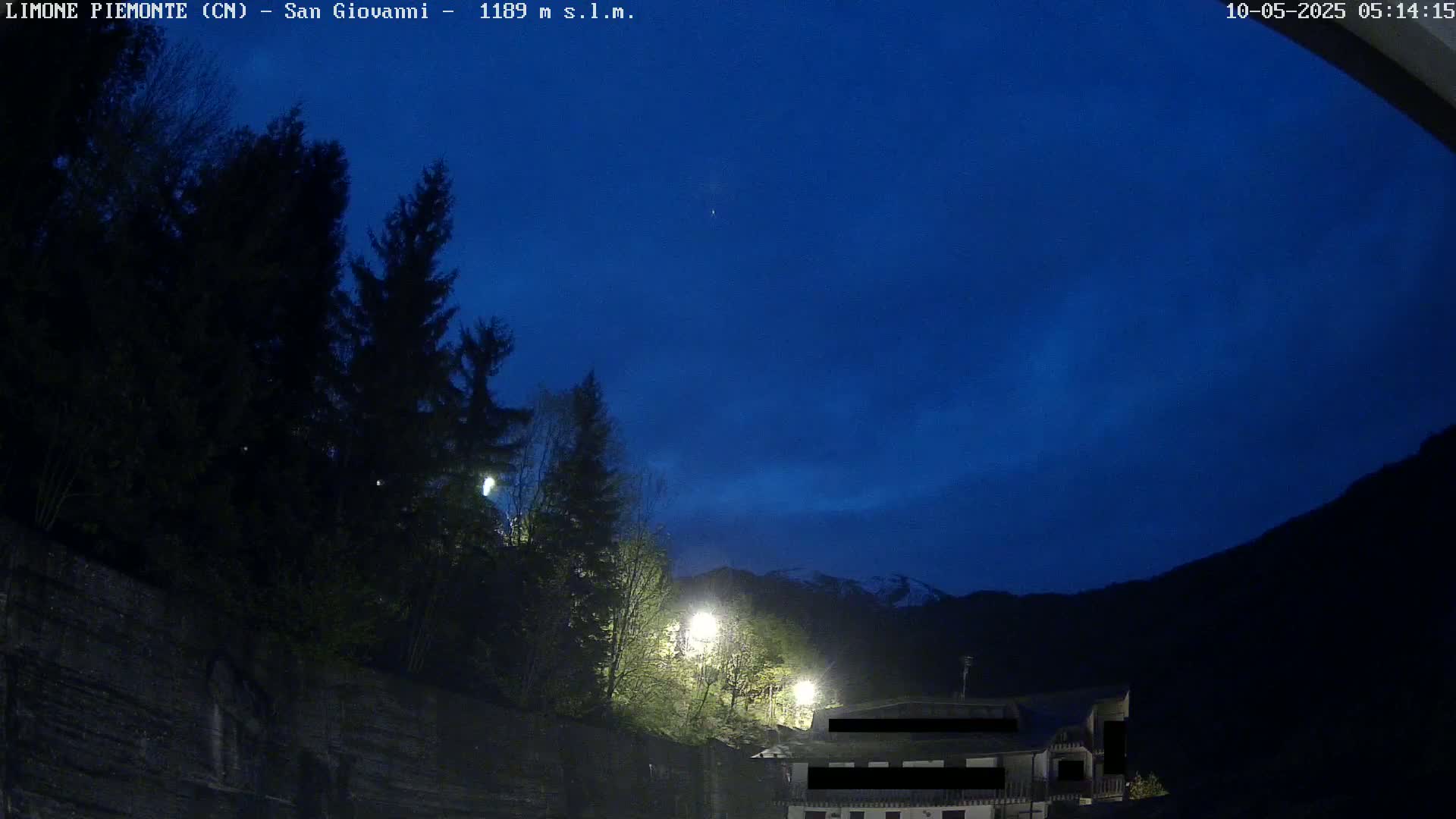 A nighttime view of a dark mountainside with a building and trees illuminated by artificial lights under a twilight sky.