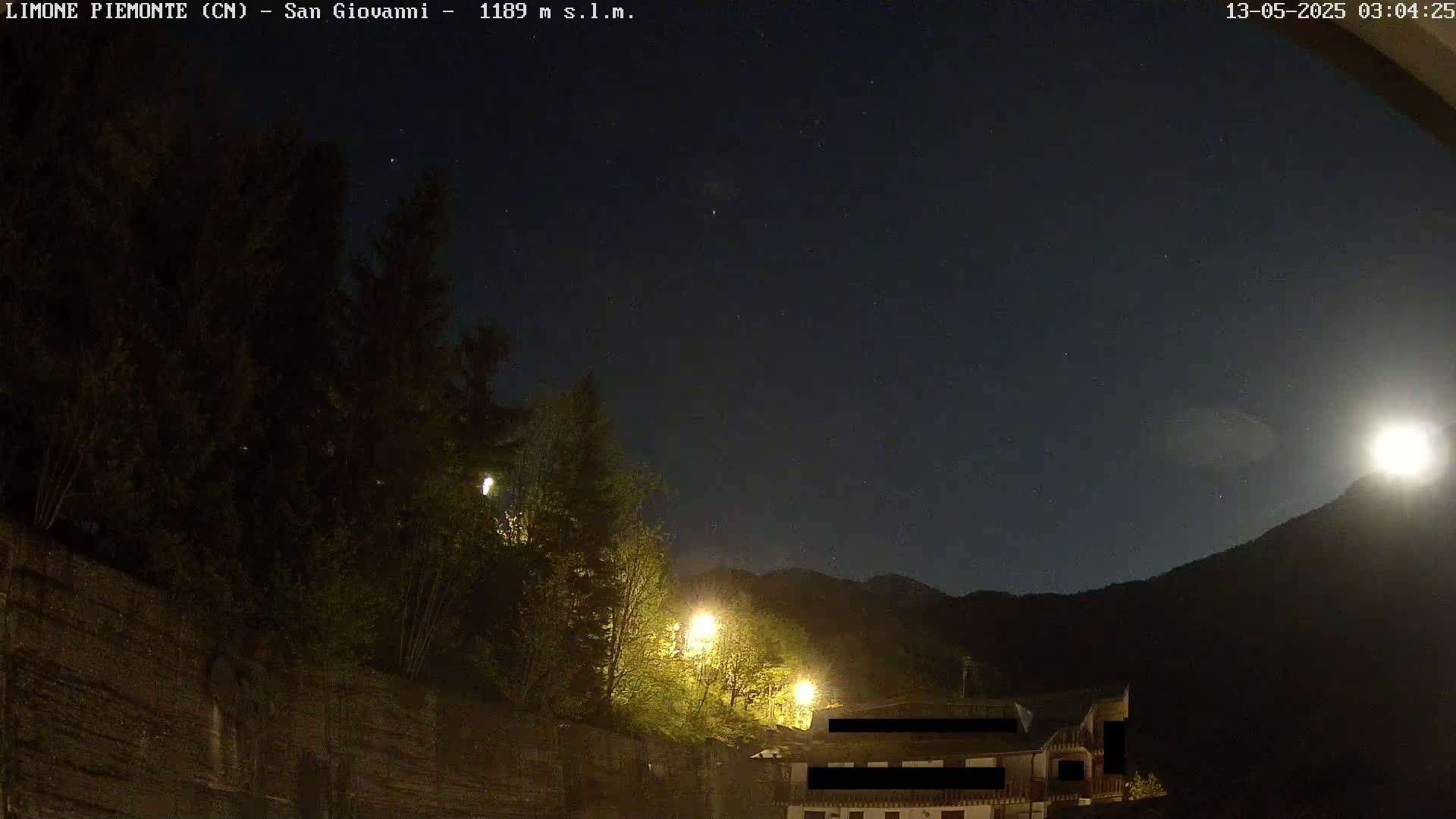 A moonlit night scene shows a building nestled amongst dark trees and a mountainside under a starry sky.