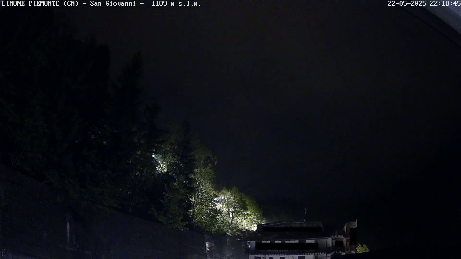 A dark nighttime scene shows a building partially obscured by trees under a mostly clear sky.