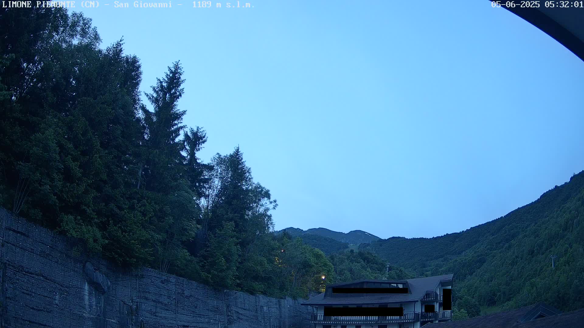 A building sits nestled in a mountainous, wooded area under a clear, twilight sky.