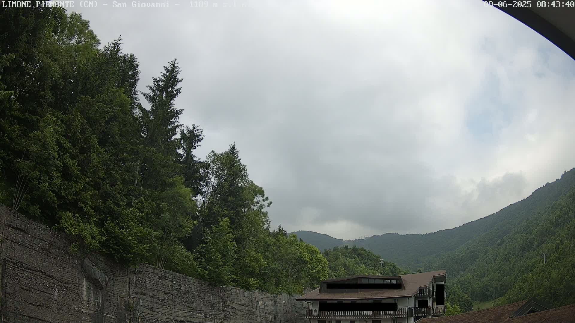 A cloudy day reveals a building nestled among lush green trees and a mountainside.