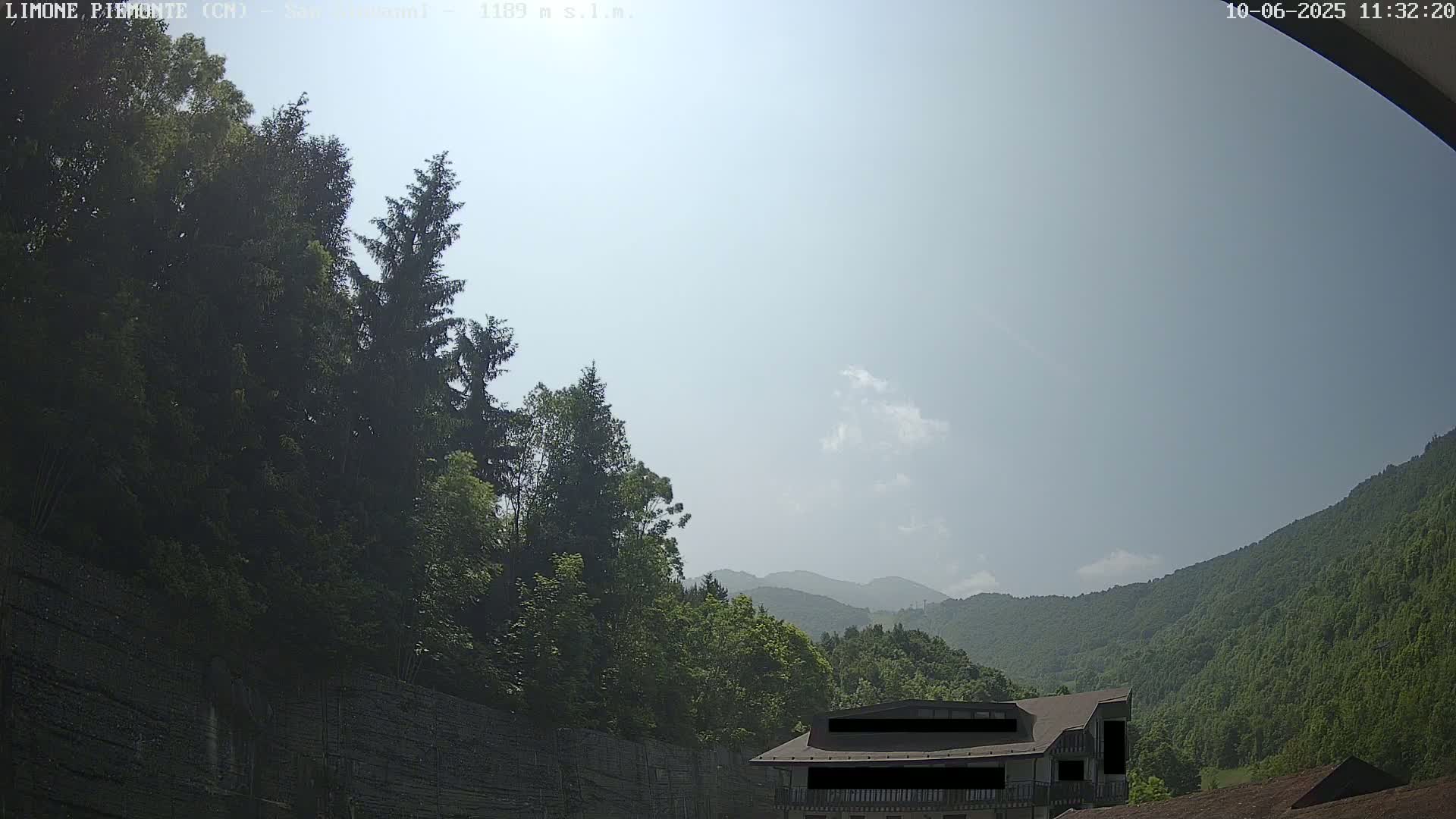 A hazy, sunny day reveals a mountainous landscape covered in lush green trees, with a building partially visible near the bottom.