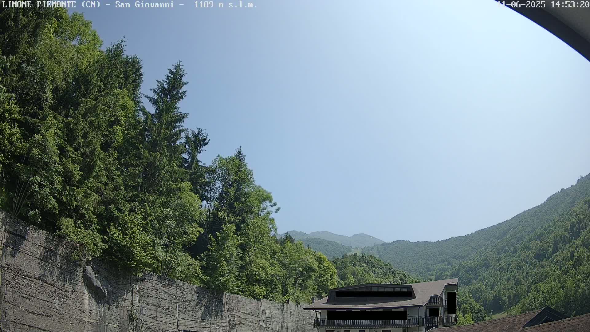 A building sits nestled among lush green trees and hills under a clear, bright blue sky.