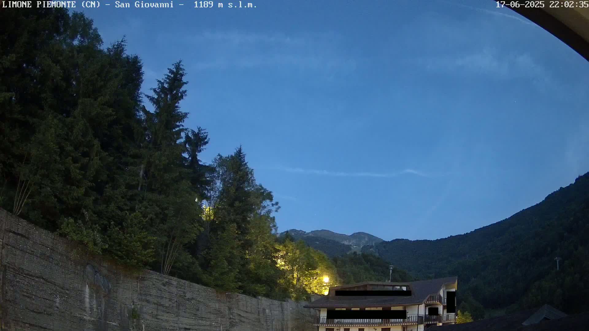 A twilight view shows a building nestled among dark green mountains under a clear blue sky.