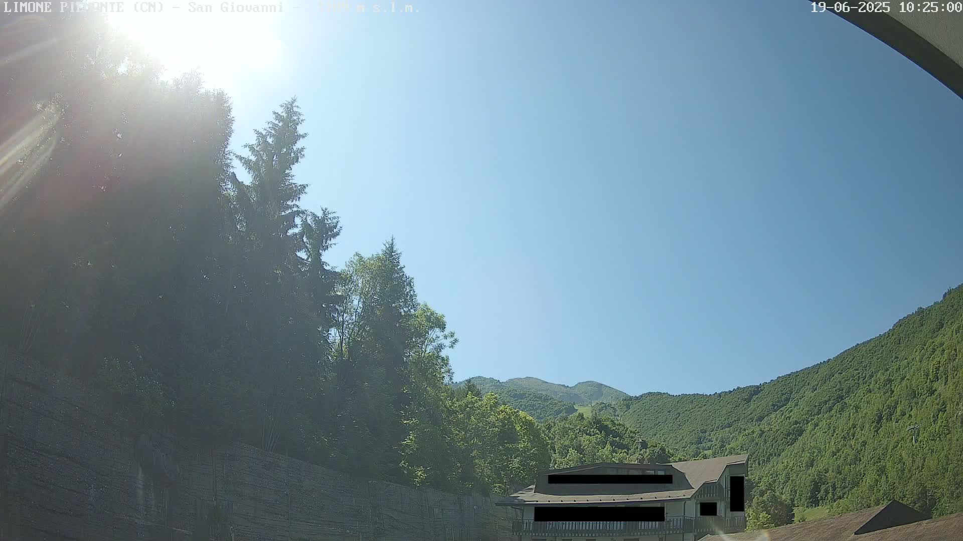 A sunny day reveals a building nestled among green, tree-covered hills and mountains.