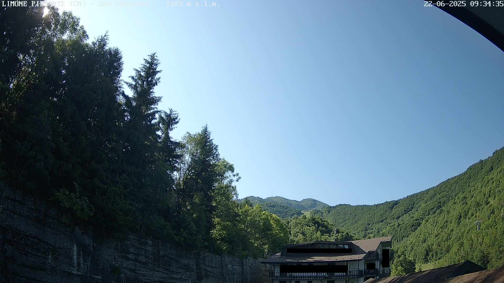 A building sits nestled in a lush green mountain valley under a clear blue sky.