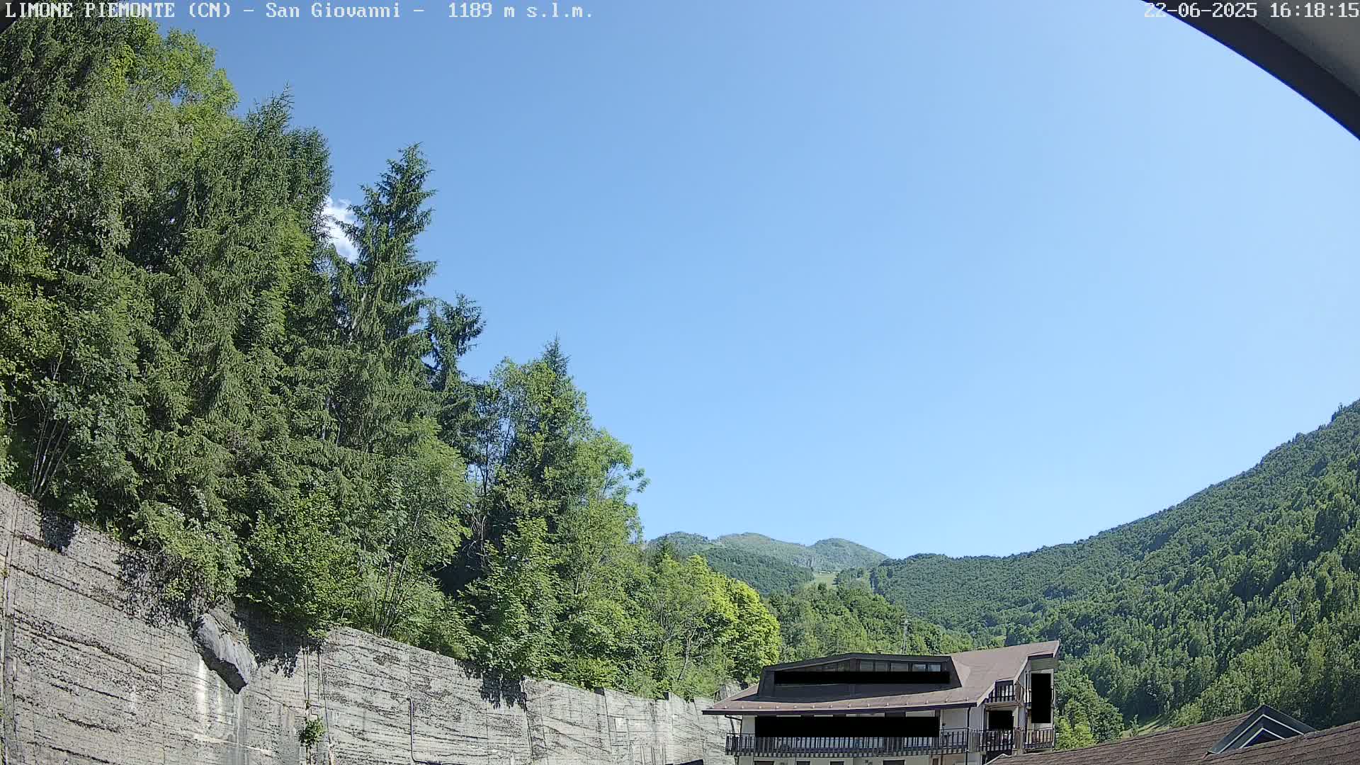 A building sits nestled among lush green trees and mountains under a clear blue sky.
