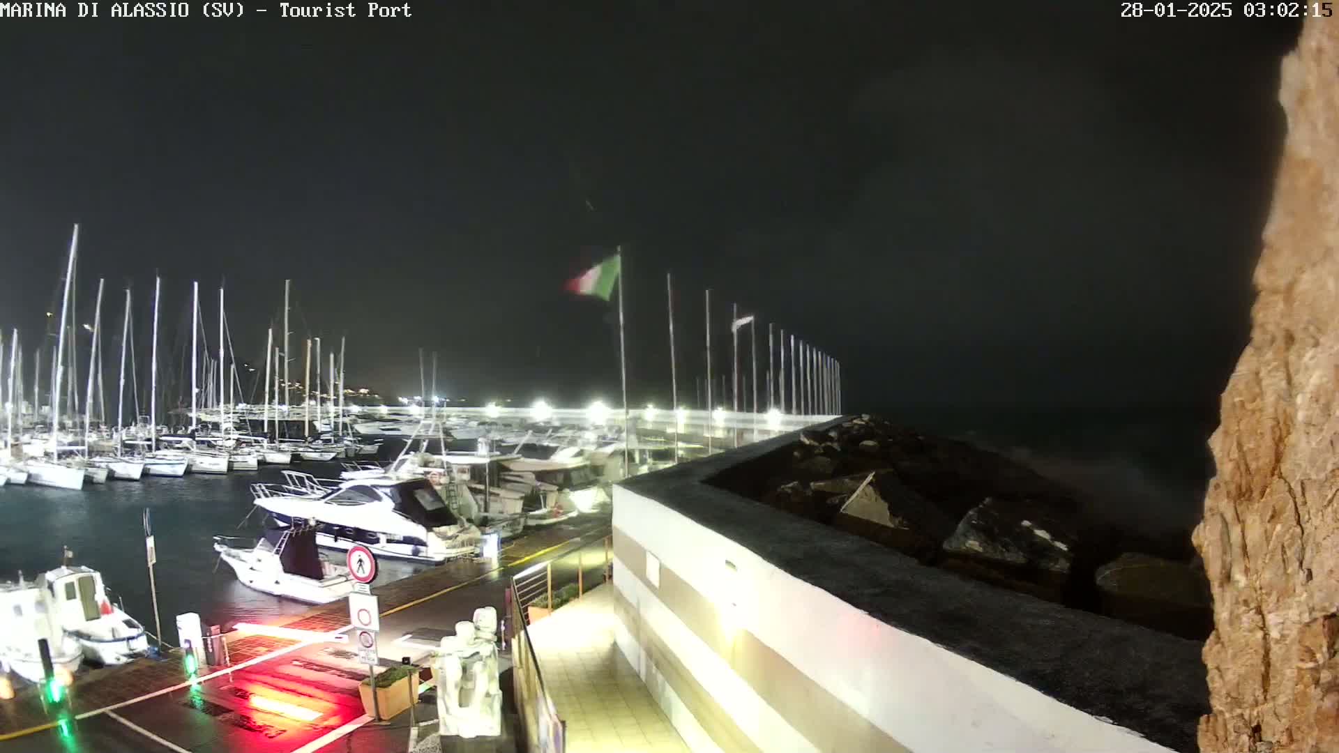 A nighttime view of a marina with numerous boats docked, under stormy conditions with strong winds.