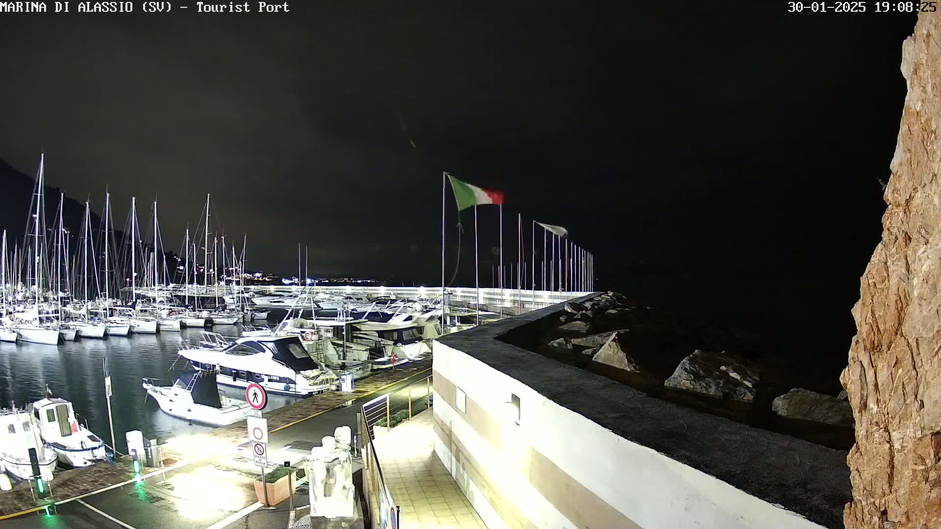 A nighttime view of a marina filled with sailboats and motorboats, under a dark sky.