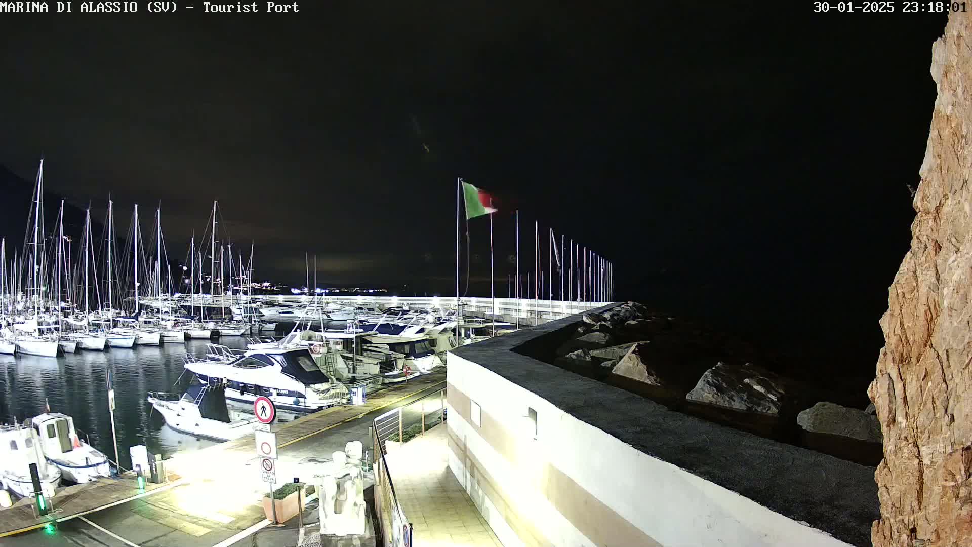 A nighttime view of a marina filled with sailboats and motorboats, under a dark sky.