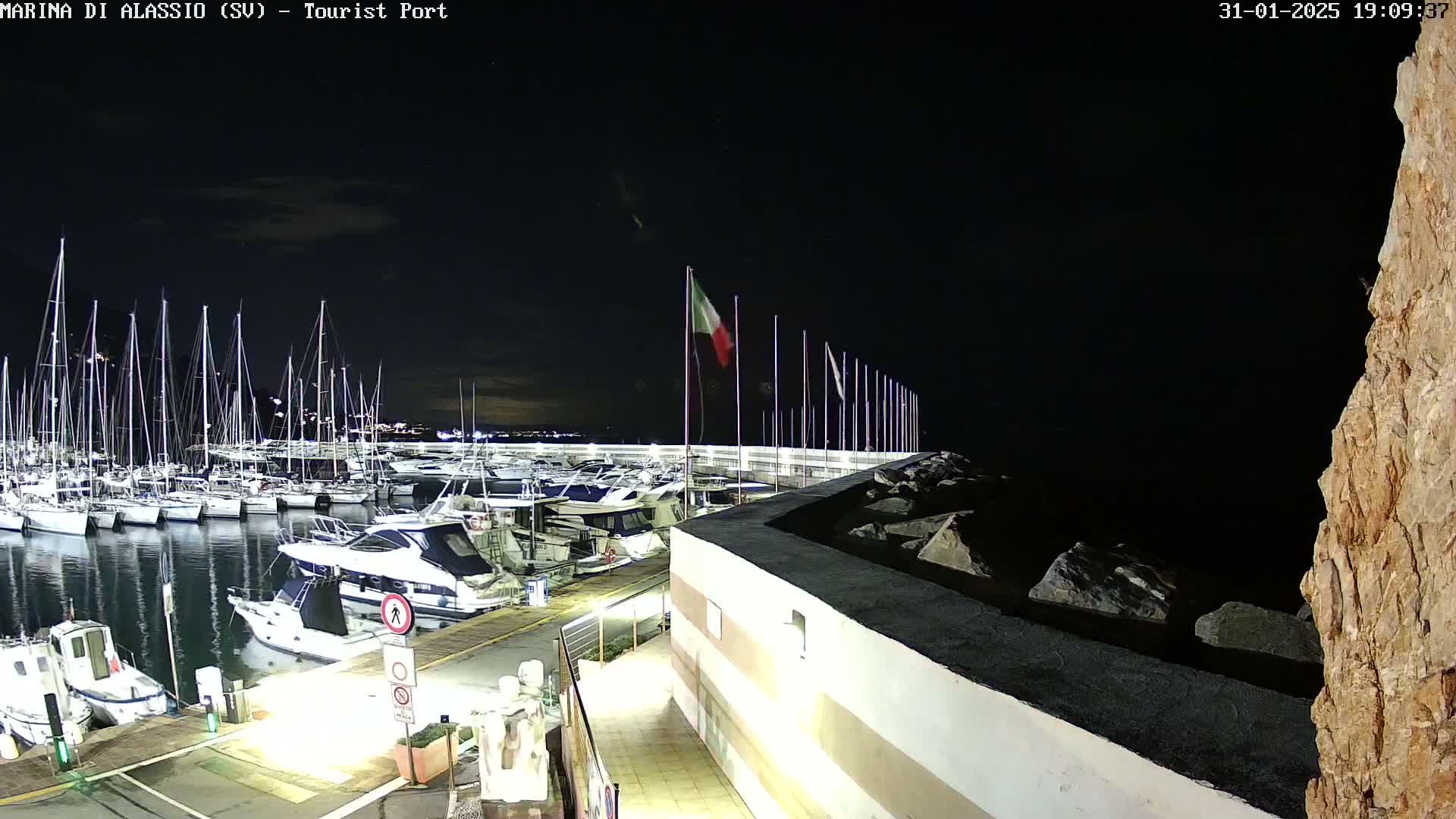 A nighttime view of a marina filled with sailboats and motorboats under a dark, clear sky.