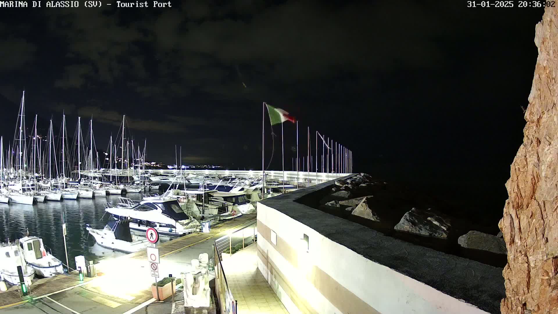A nighttime view of a marina filled with sailboats and motorboats, under a dark, cloudy sky.