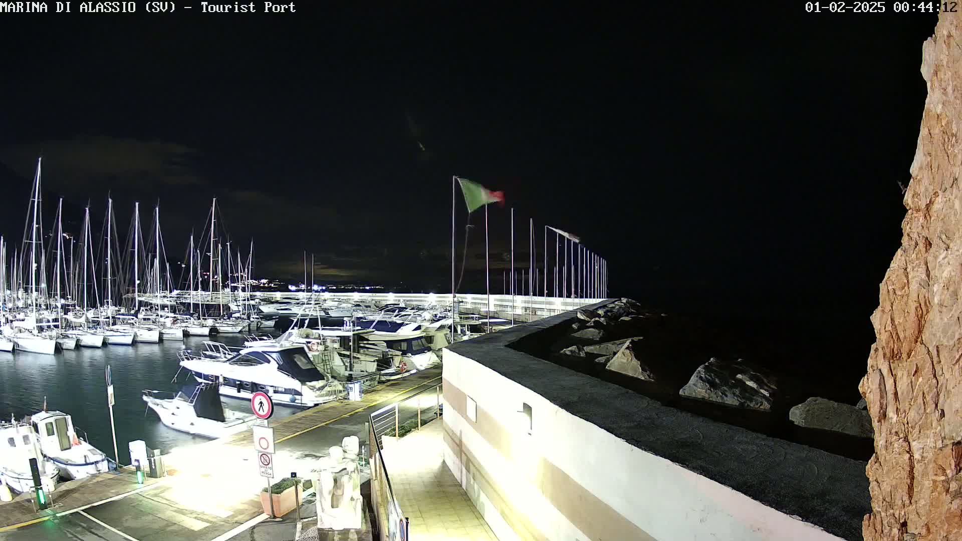 A nighttime view of a marina filled with sailboats and motorboats, under a mostly clear sky.