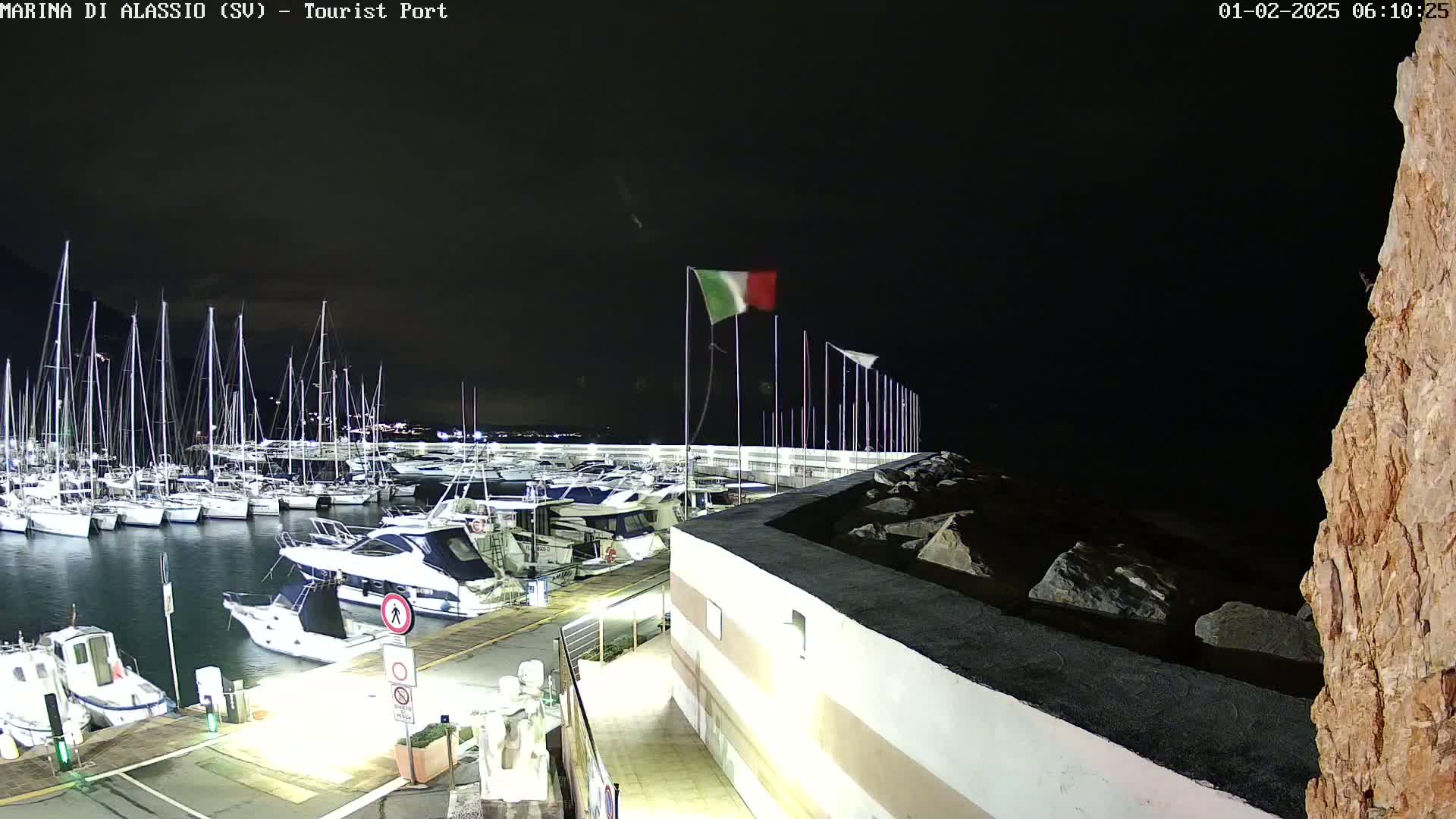A marina at night, filled with sailboats and motorboats, is illuminated under a dark sky.