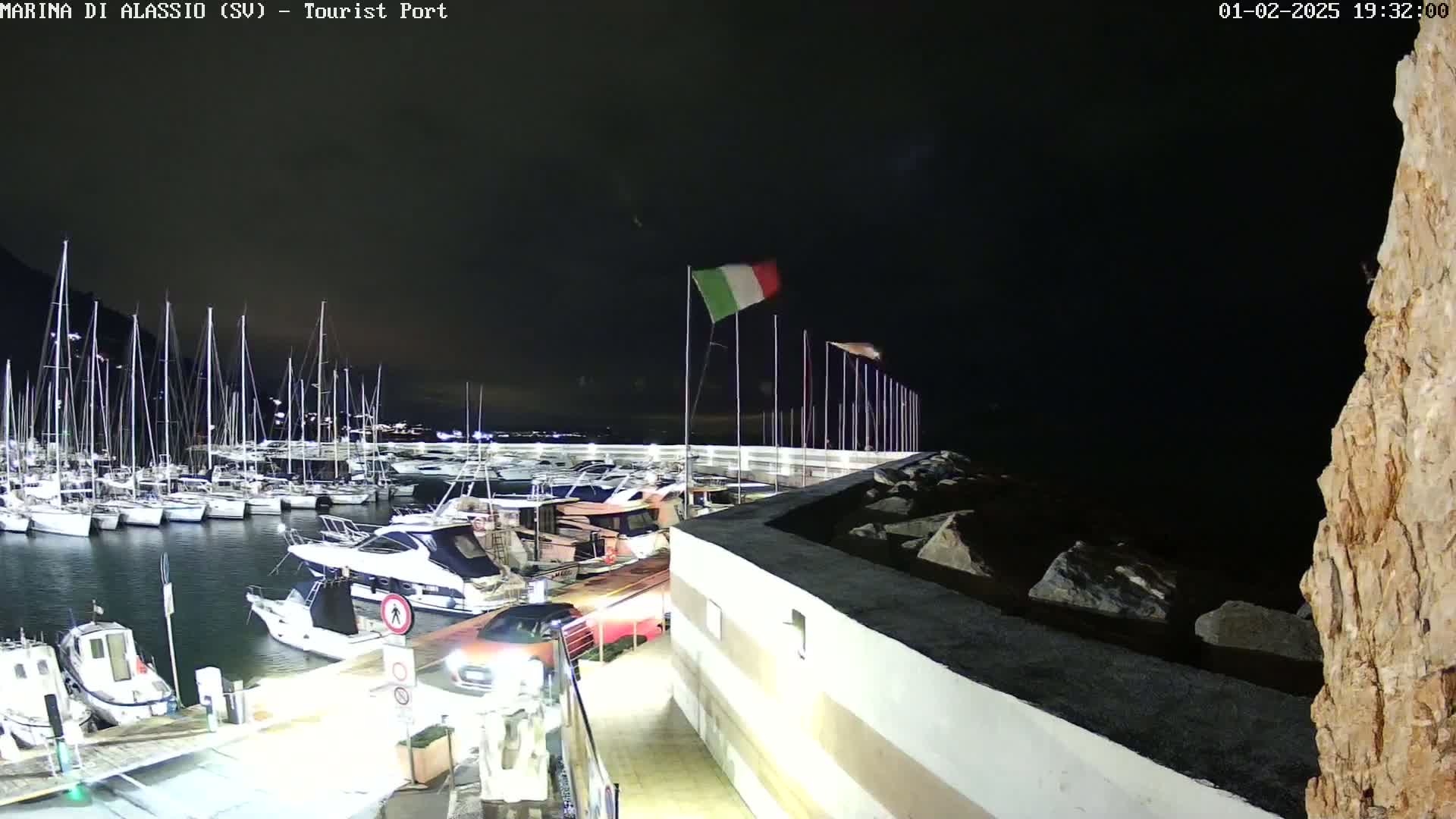 A nighttime view of a marina filled with sailboats and motorboats, under a dark sky.