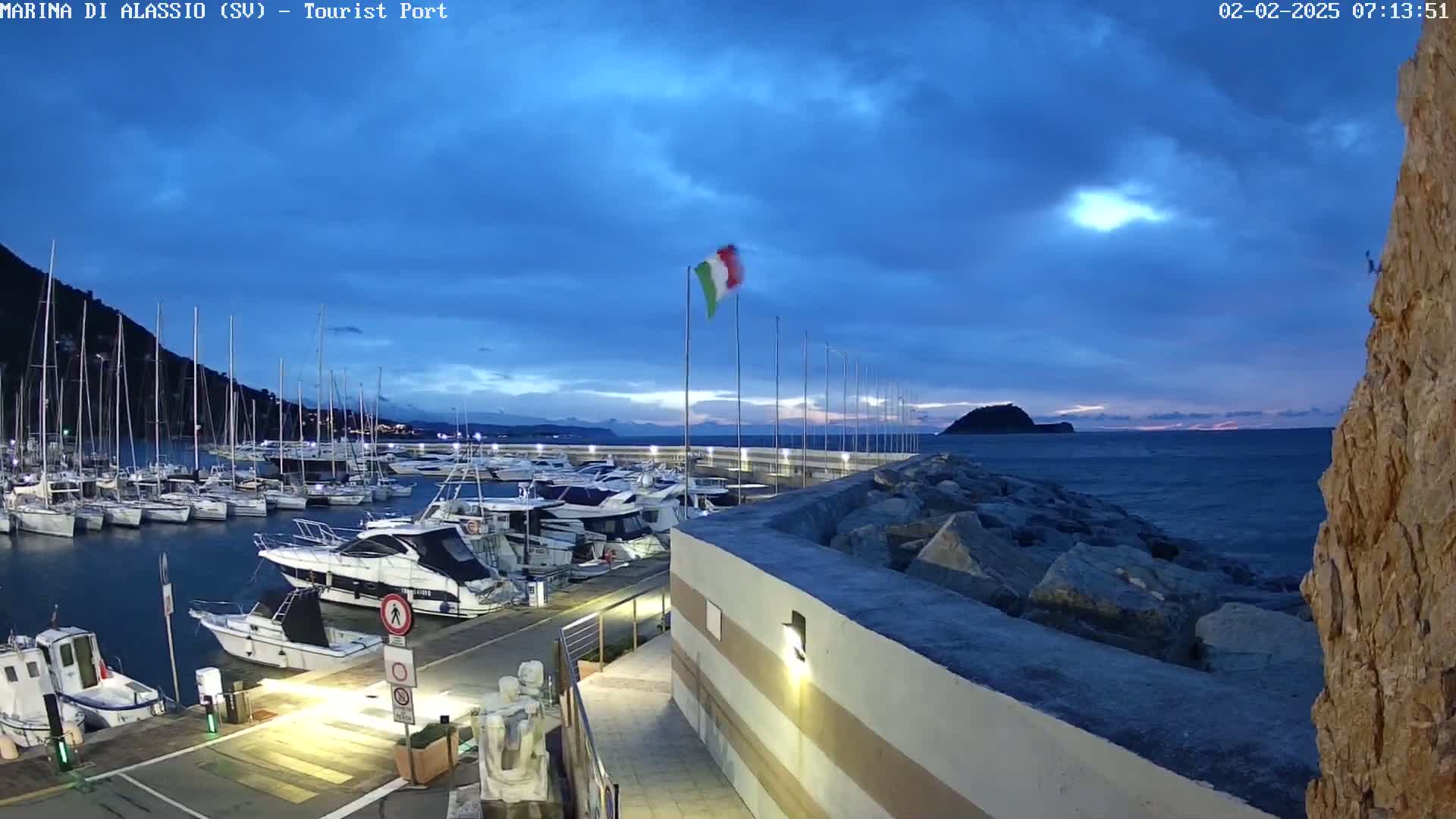 A marina filled with sailboats and motorboats is seen at twilight under a partly cloudy sky.