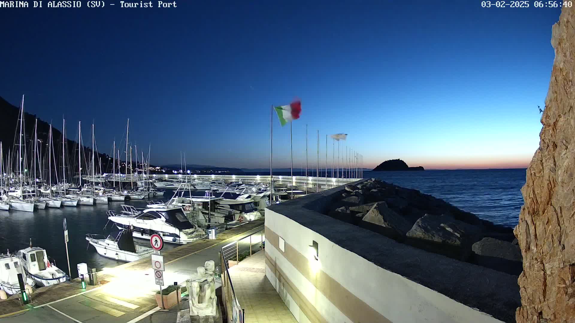 A marina filled with sailboats and motorboats at dusk under a clear, dark blue sky.