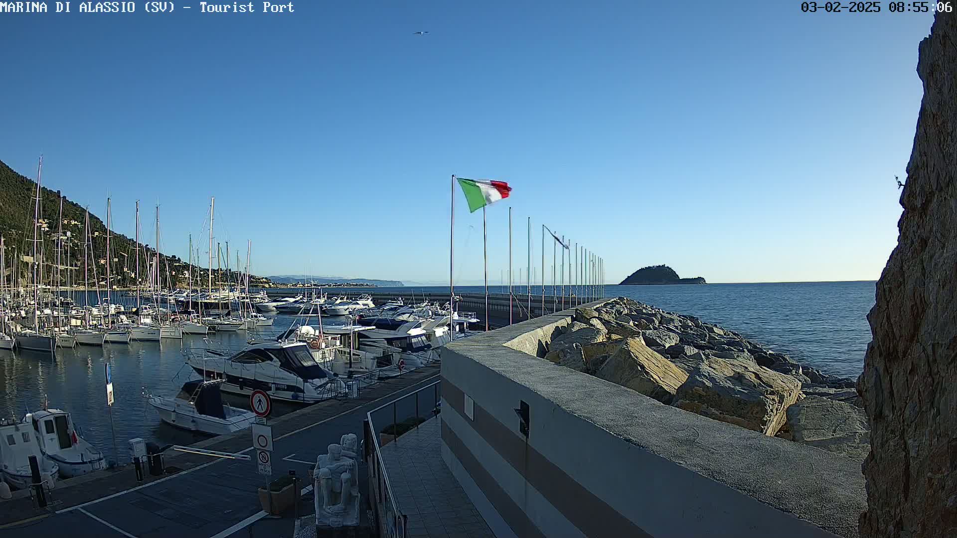A harbor filled with boats is situated next to a rocky coast under a clear blue sky.