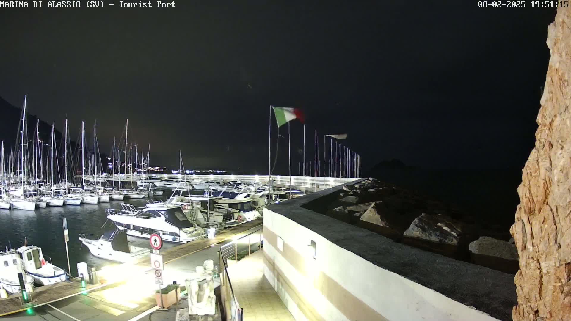 A nighttime view of a marina filled with sailboats and motorboats, under a dark sky.
