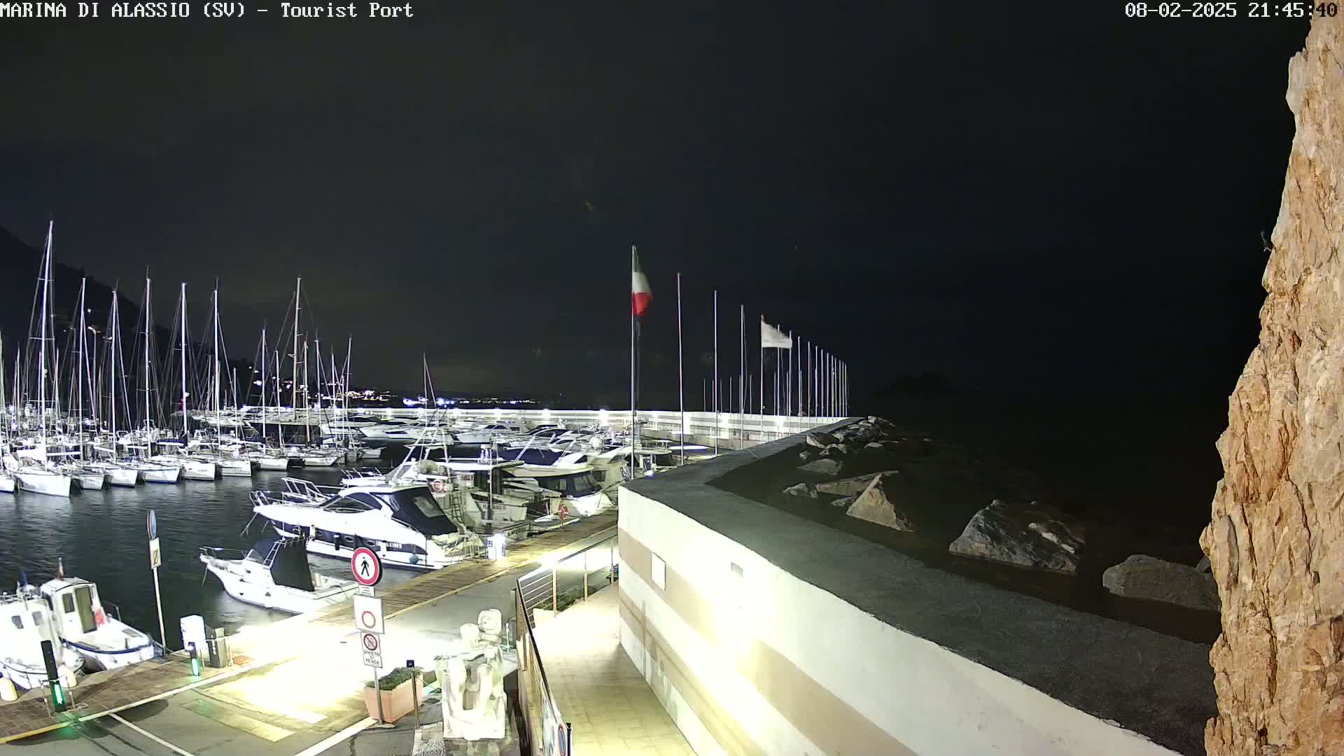 A nighttime view of a marina filled with sailboats and motorboats, illuminated under a dark sky.