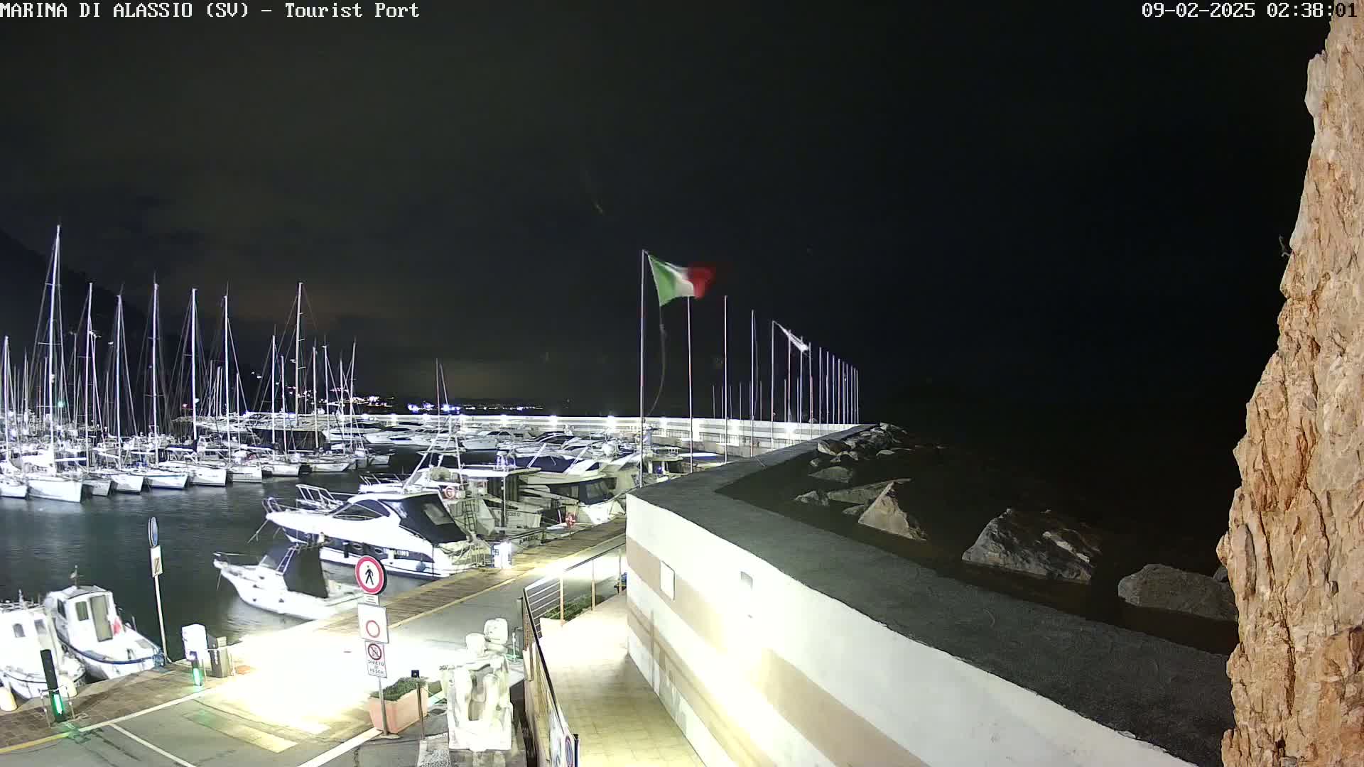 A nighttime view of a marina filled with sailboats and motorboats, under a dark sky.