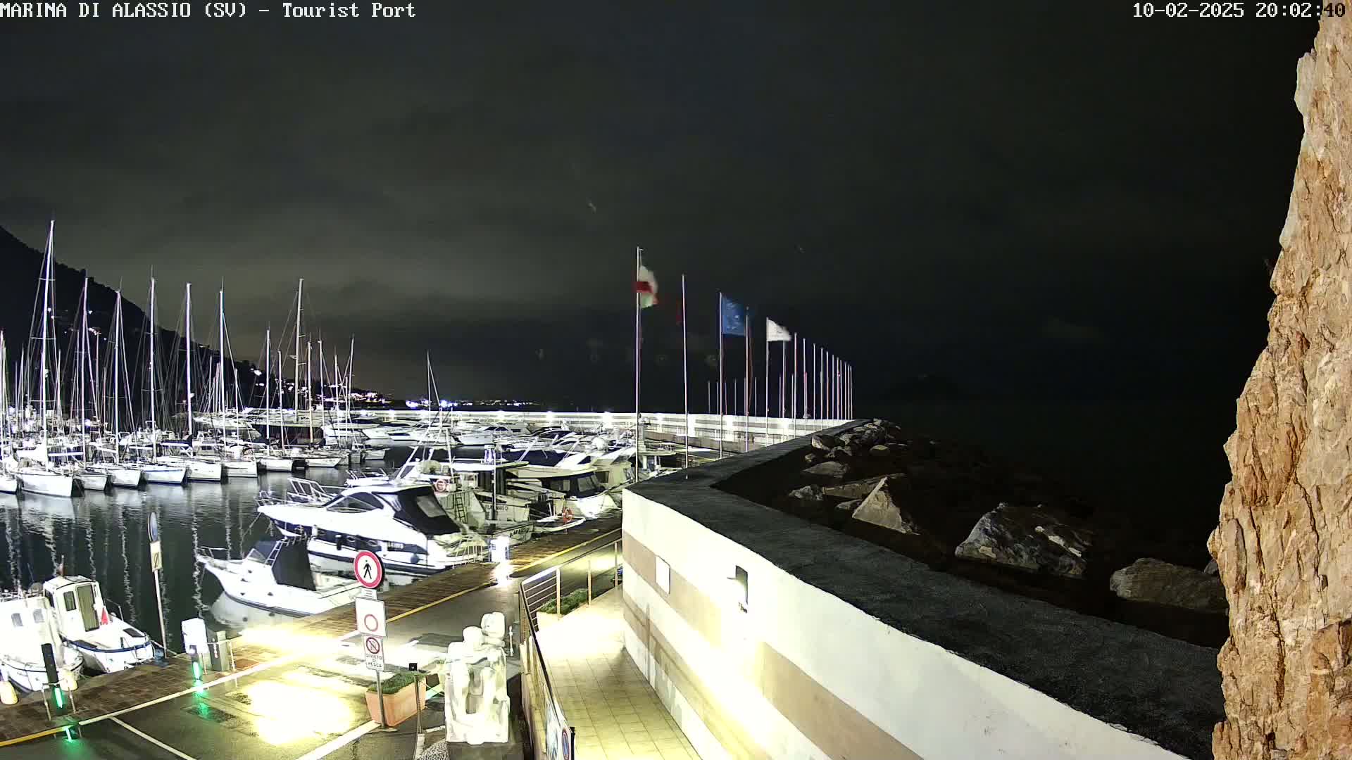 A nighttime view of a marina filled with sailboats and motorboats under a dark, cloudy sky.