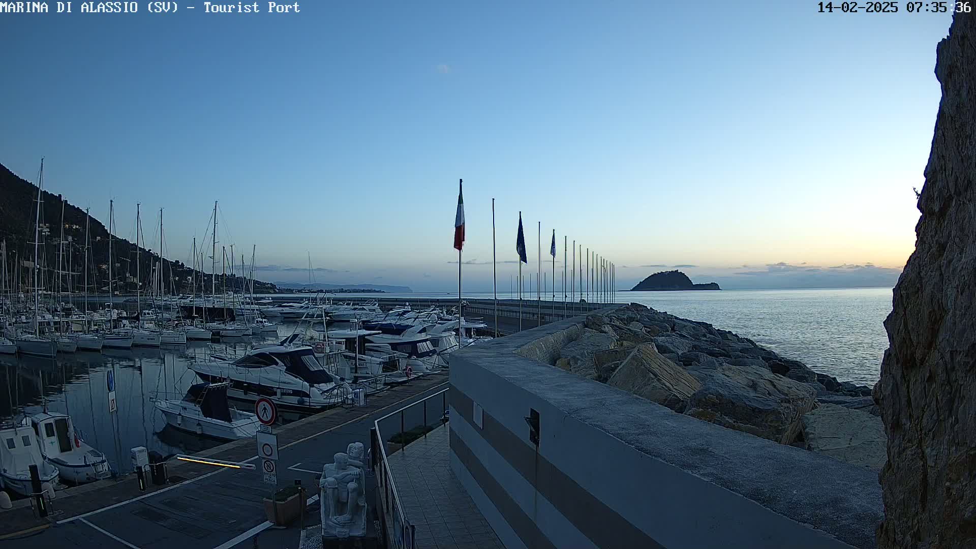 A calm harbor filled with yachts and sailboats at sunrise, under a clear, light blue sky.