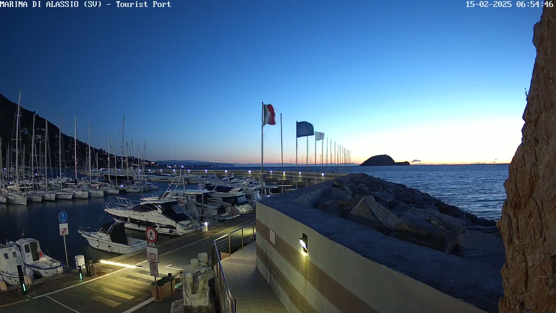 A marina filled with sailboats and motorboats at twilight under a clear, dark blue sky.