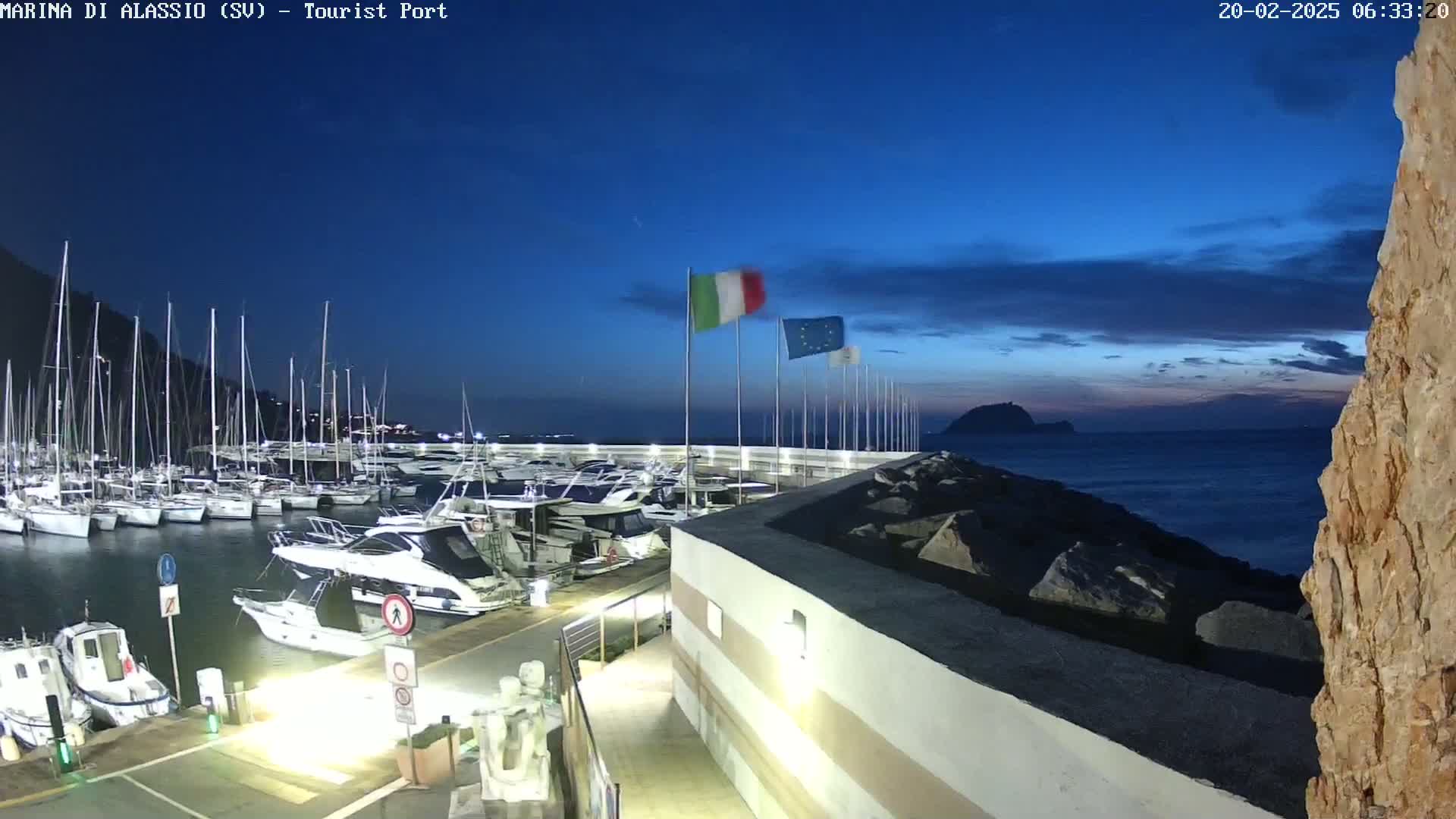 A marina filled with yachts and sailboats is seen at twilight under a mostly clear, dark blue sky.