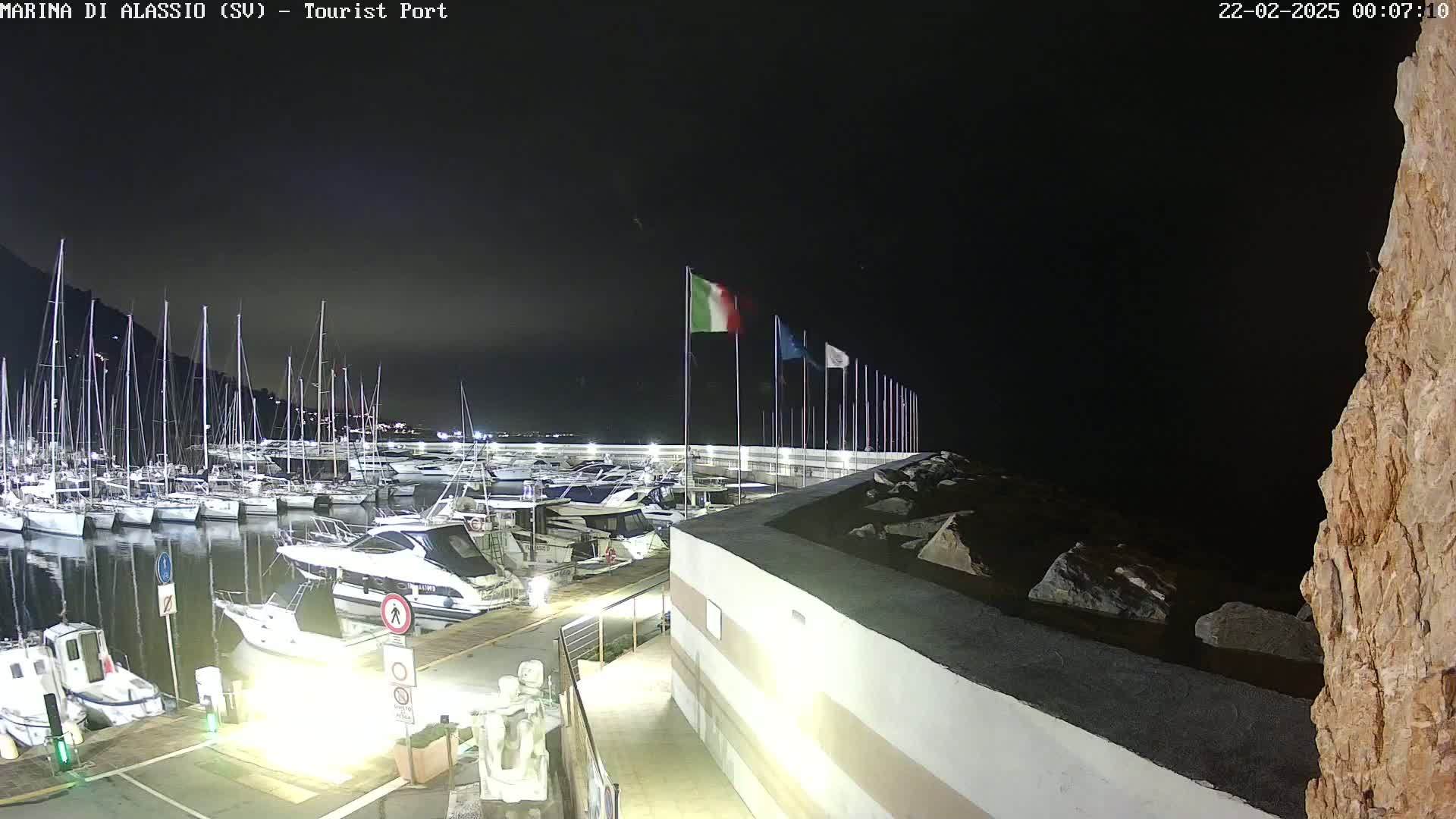 A nighttime view of a marina filled with boats docked alongside a seawall, under a dark sky.