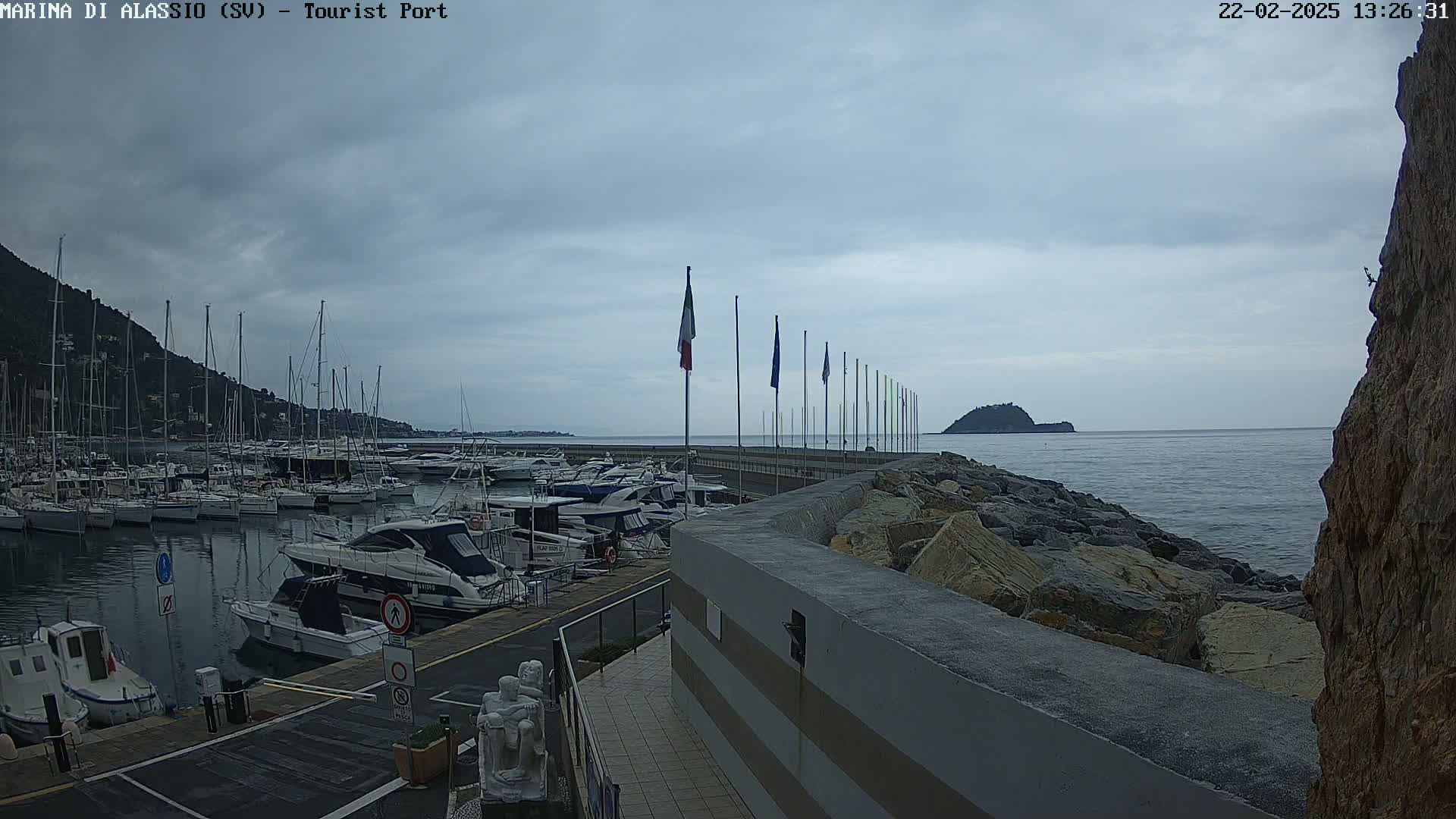 A harbor filled with boats is situated next to a rocky coast under a cloudy sky.