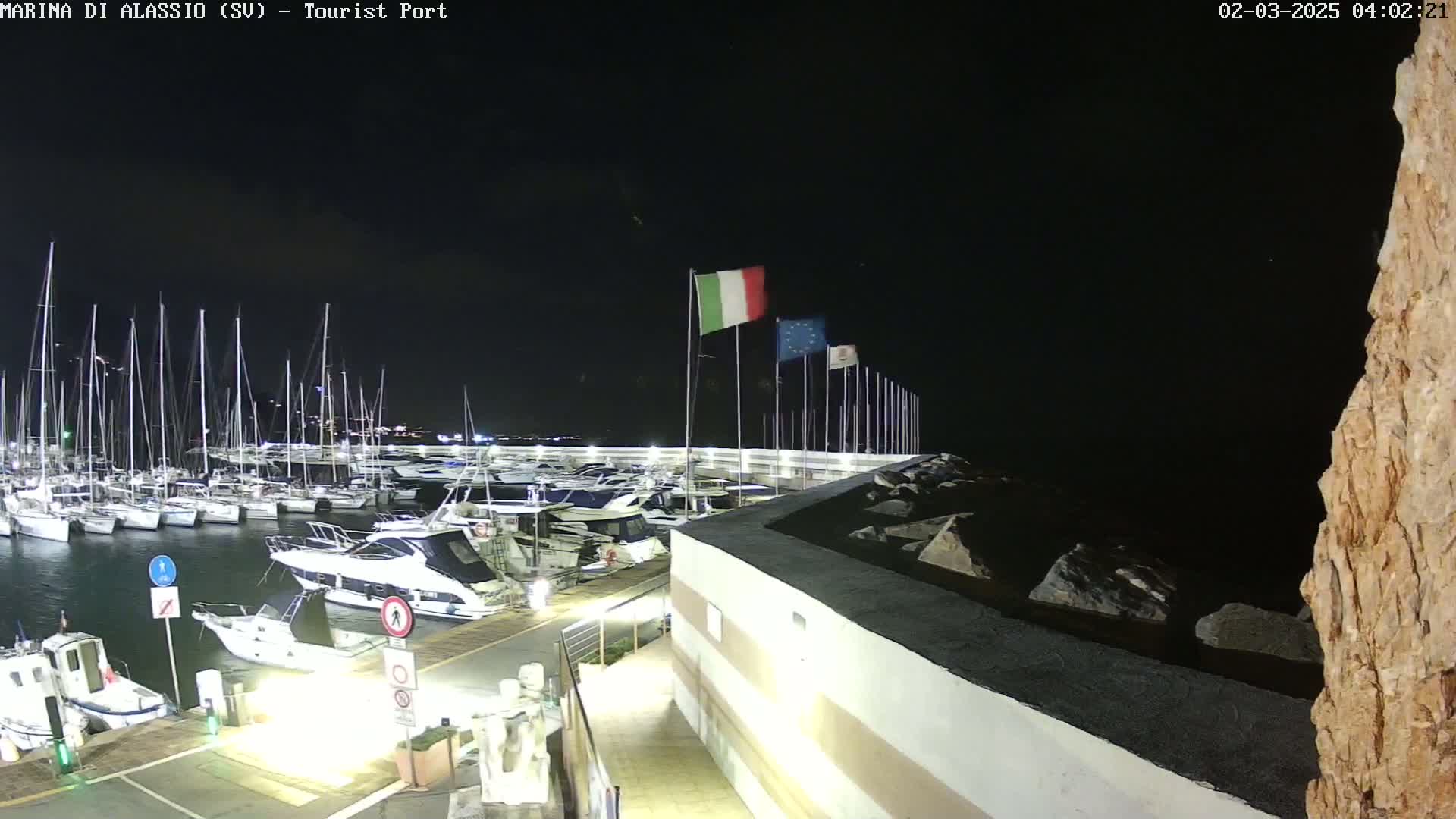 A nighttime view of a marina filled with sailboats and motorboats, under a clear, dark sky.