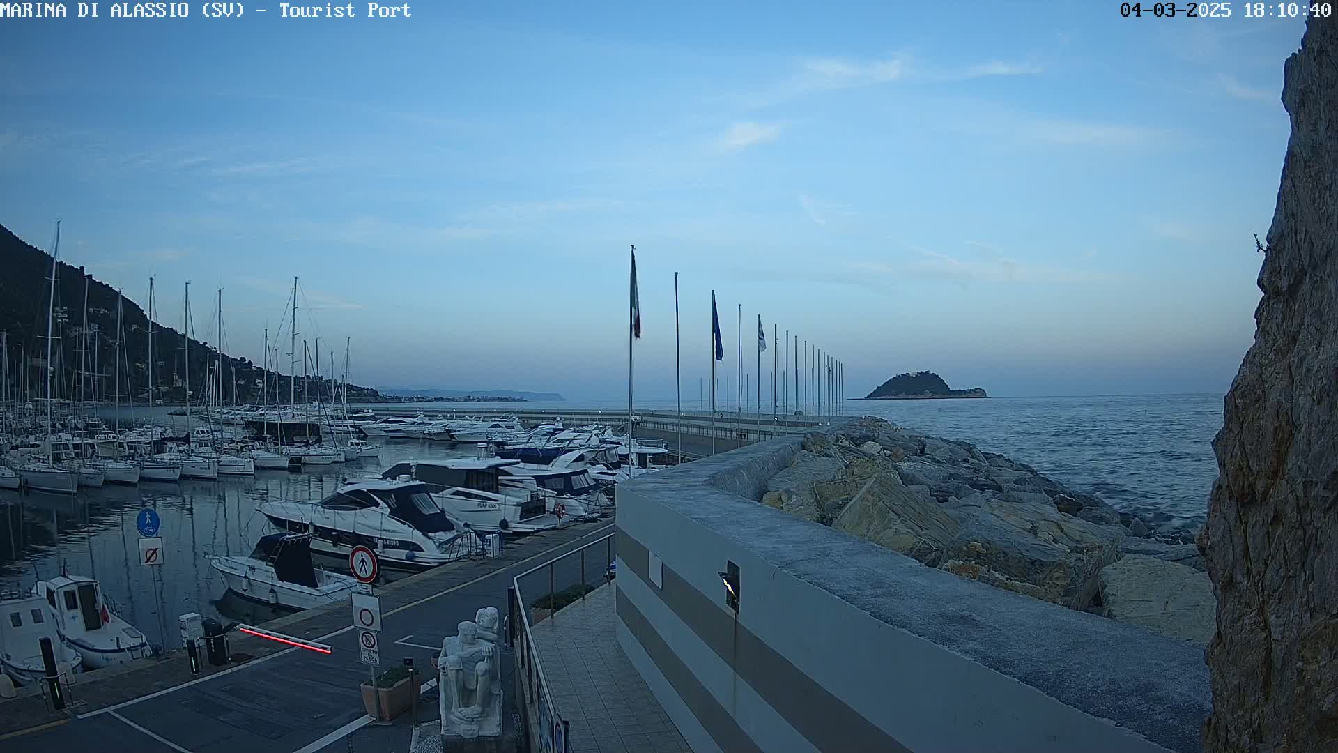 A marina filled with boats is nestled beside a rocky shoreline under a twilight sky.