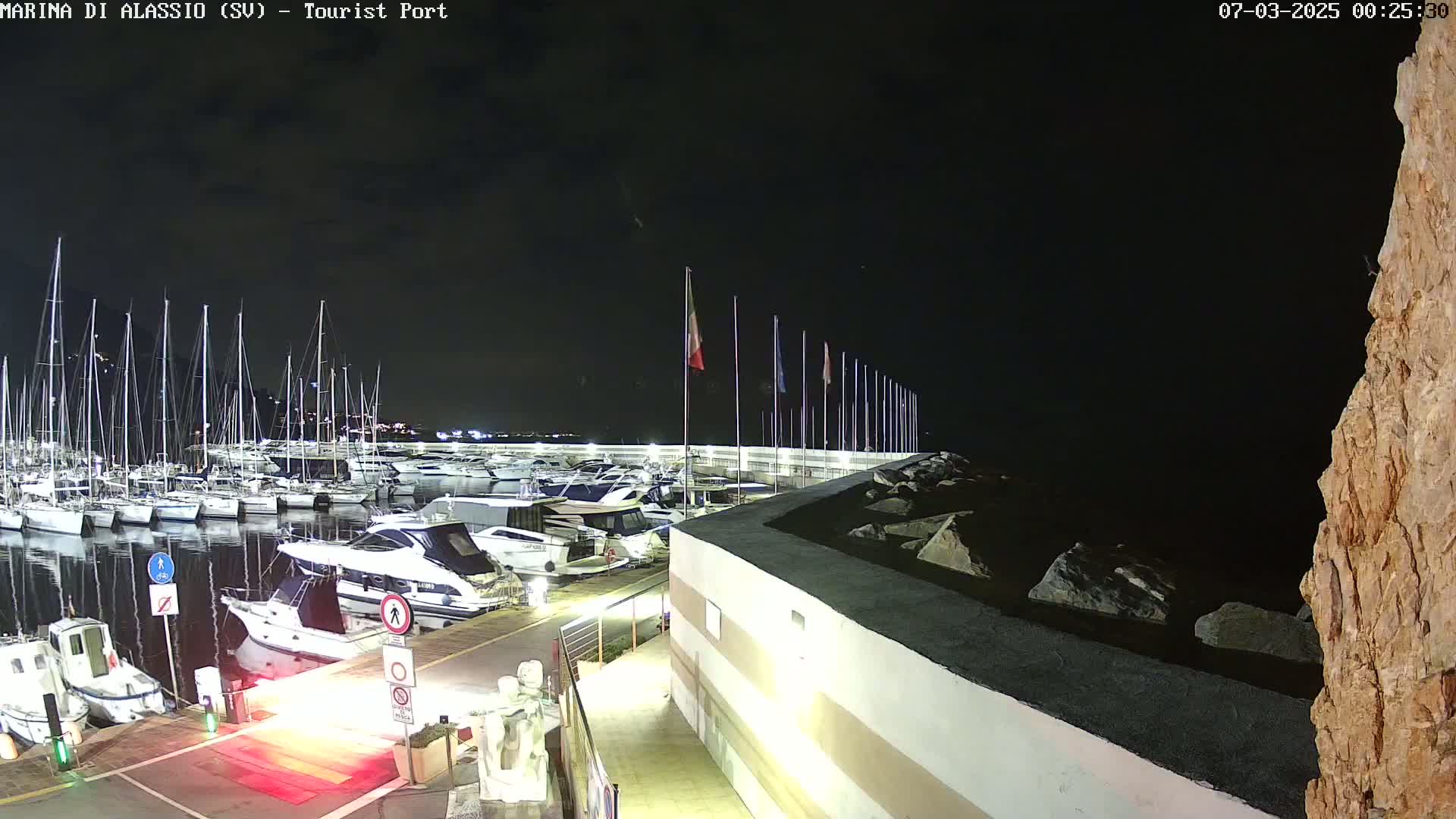 A nighttime view of a marina filled with boats docked along a seawall, under a dark sky.