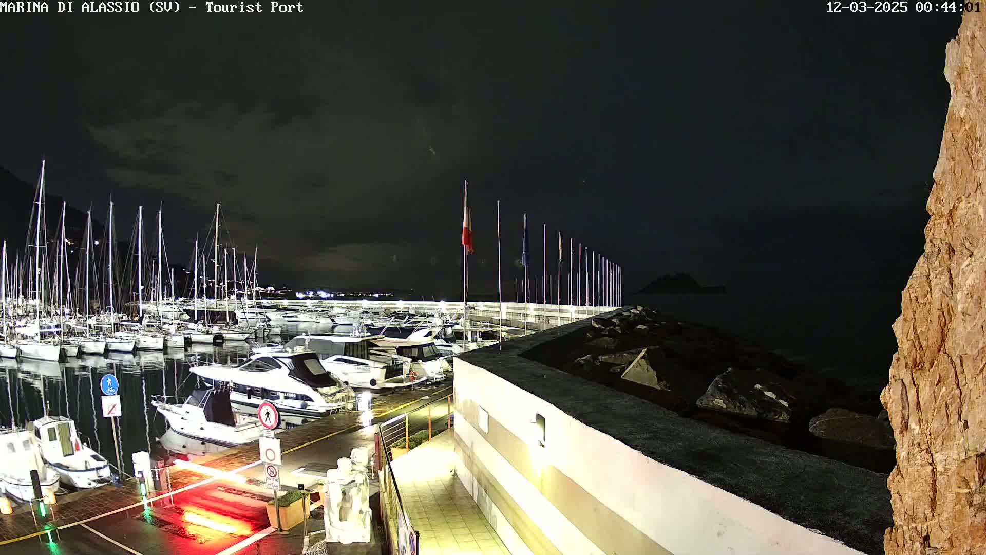 A nighttime view of a marina filled with sailboats and motorboats, under a dark, cloudy sky.