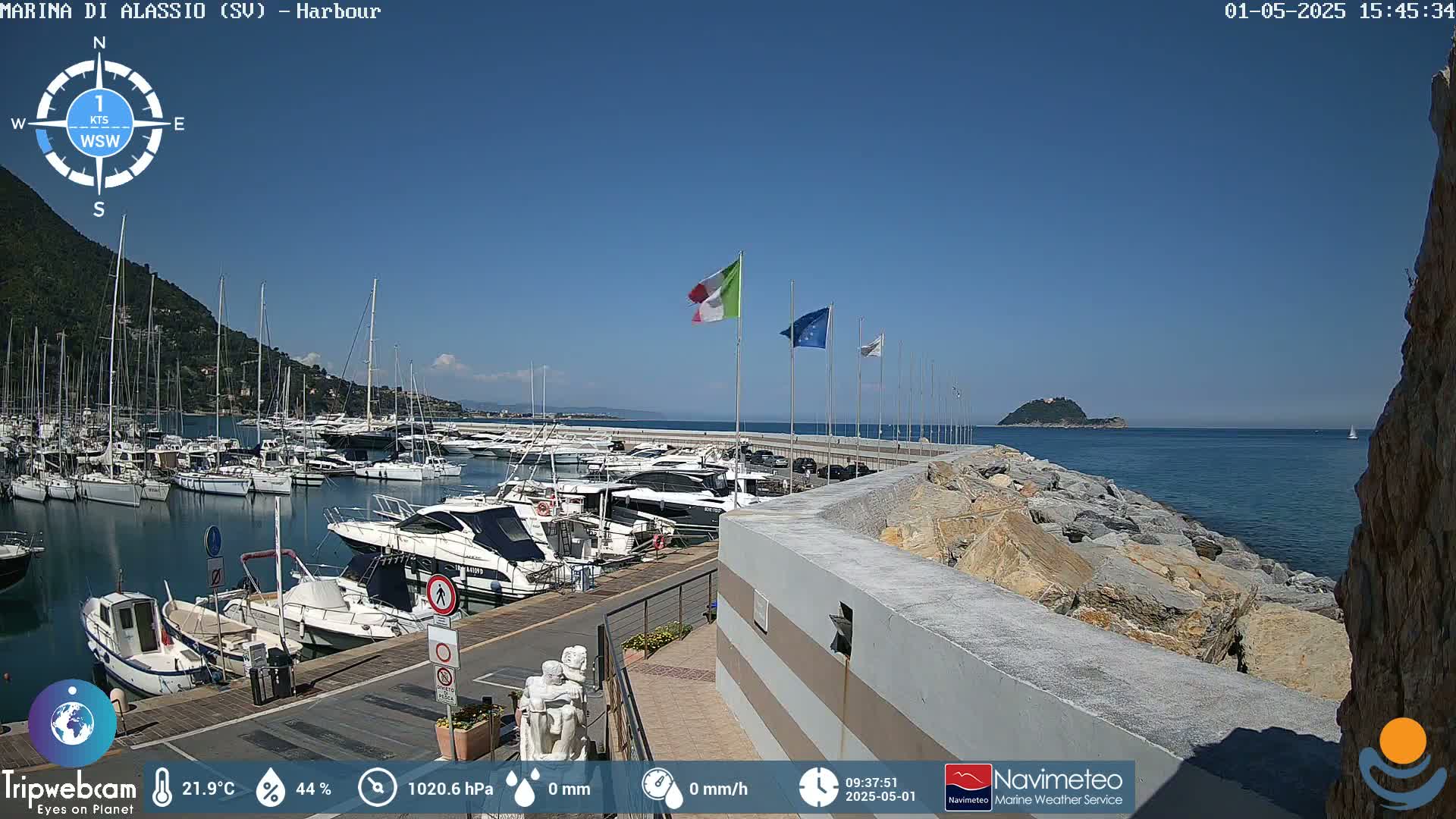A harbor filled with numerous boats is shown on a sunny day, with a small island visible in the distance.