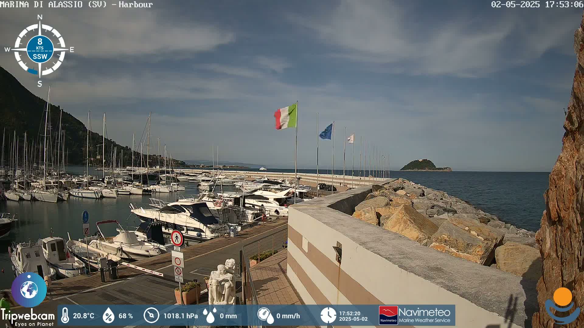 A harbor filled with numerous boats is situated beside a rocky shoreline on a partly sunny day with a gentle south-southwesterly breeze.