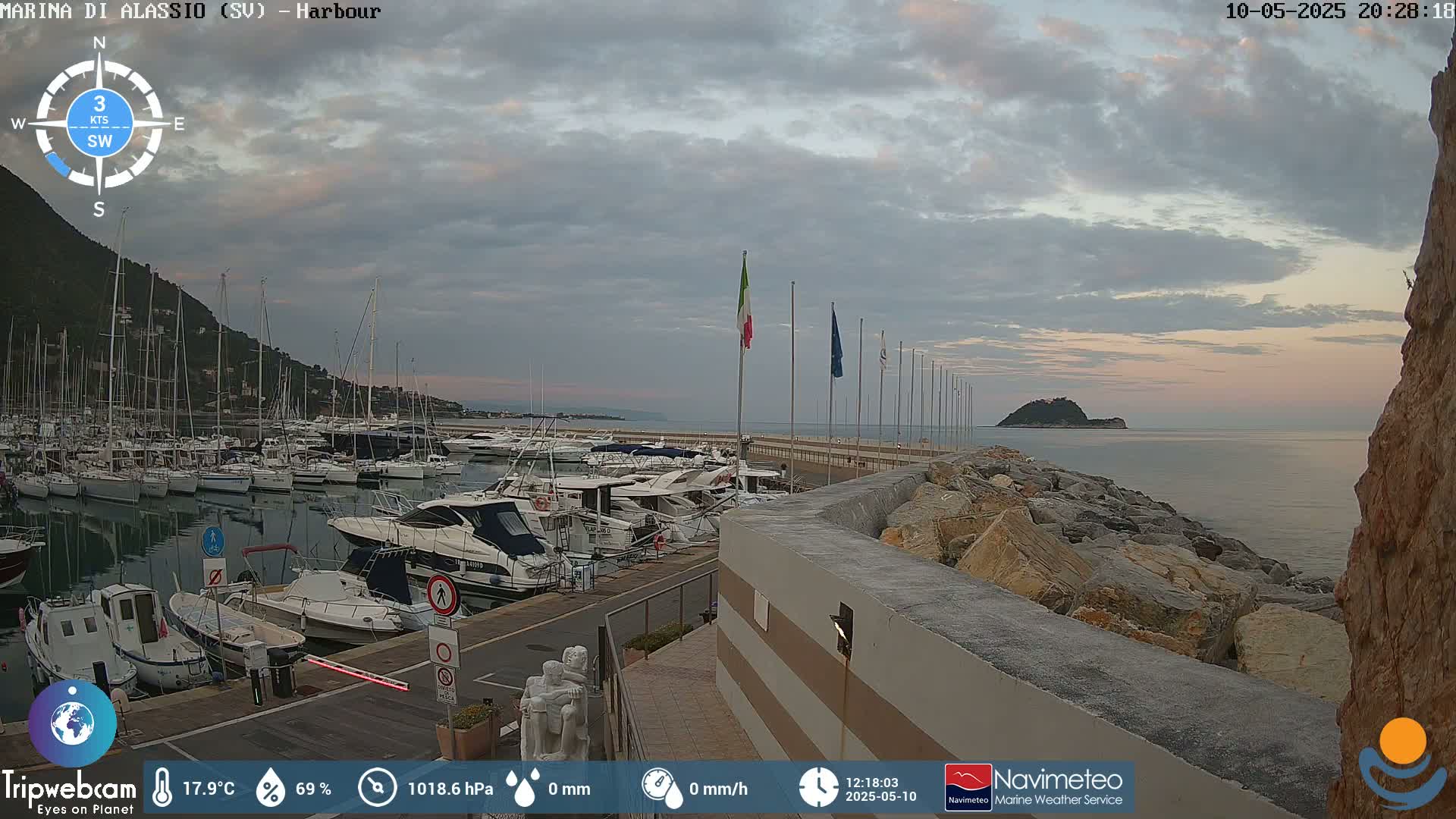 A harbor filled with numerous boats is situated next to a rocky shore under a cloudy, twilight sky.