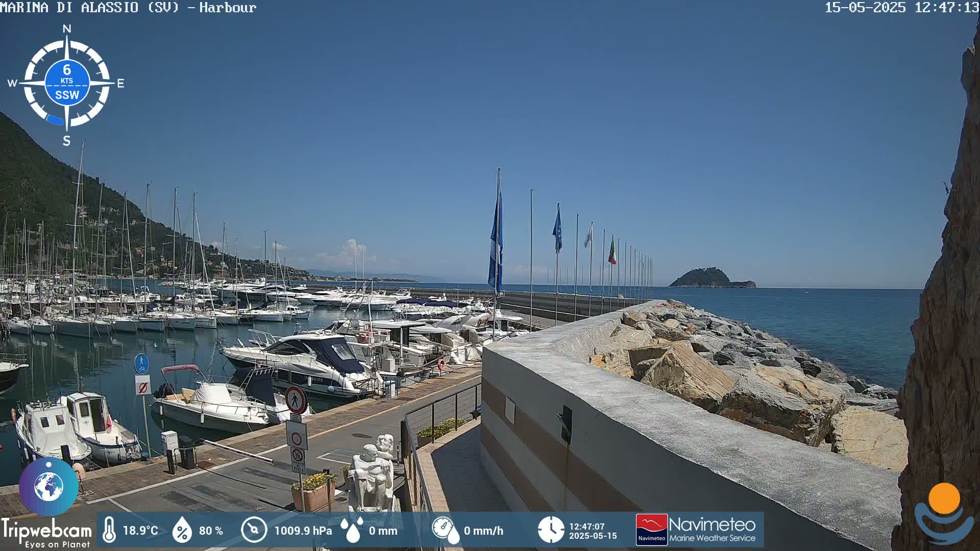 A harbor filled with boats is situated next to a rocky shoreline under a clear blue sky.