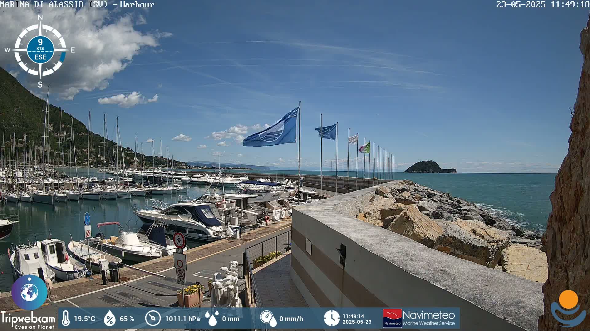 A harbor filled with boats is situated next to a rocky shoreline under a mostly sunny sky with a few scattered clouds.