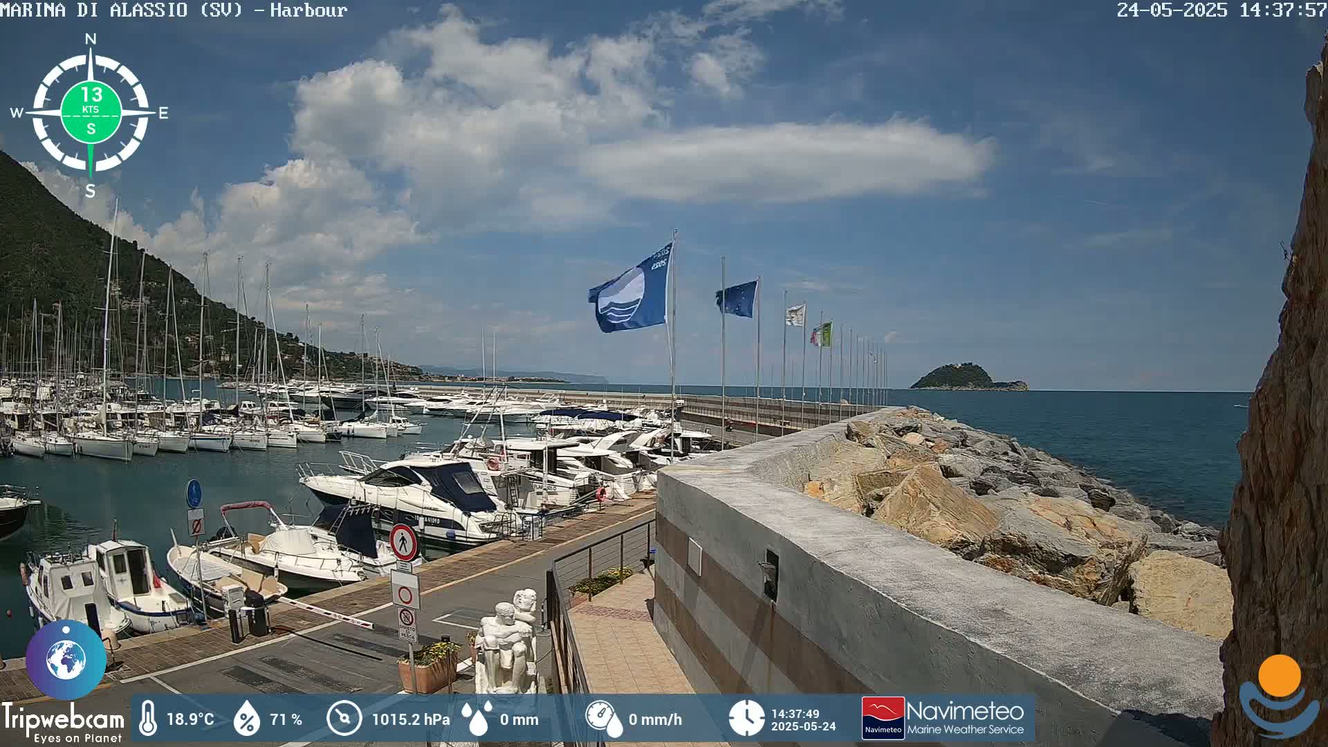 A harbor filled with numerous boats is nestled beside a rocky shoreline on a partly cloudy day.