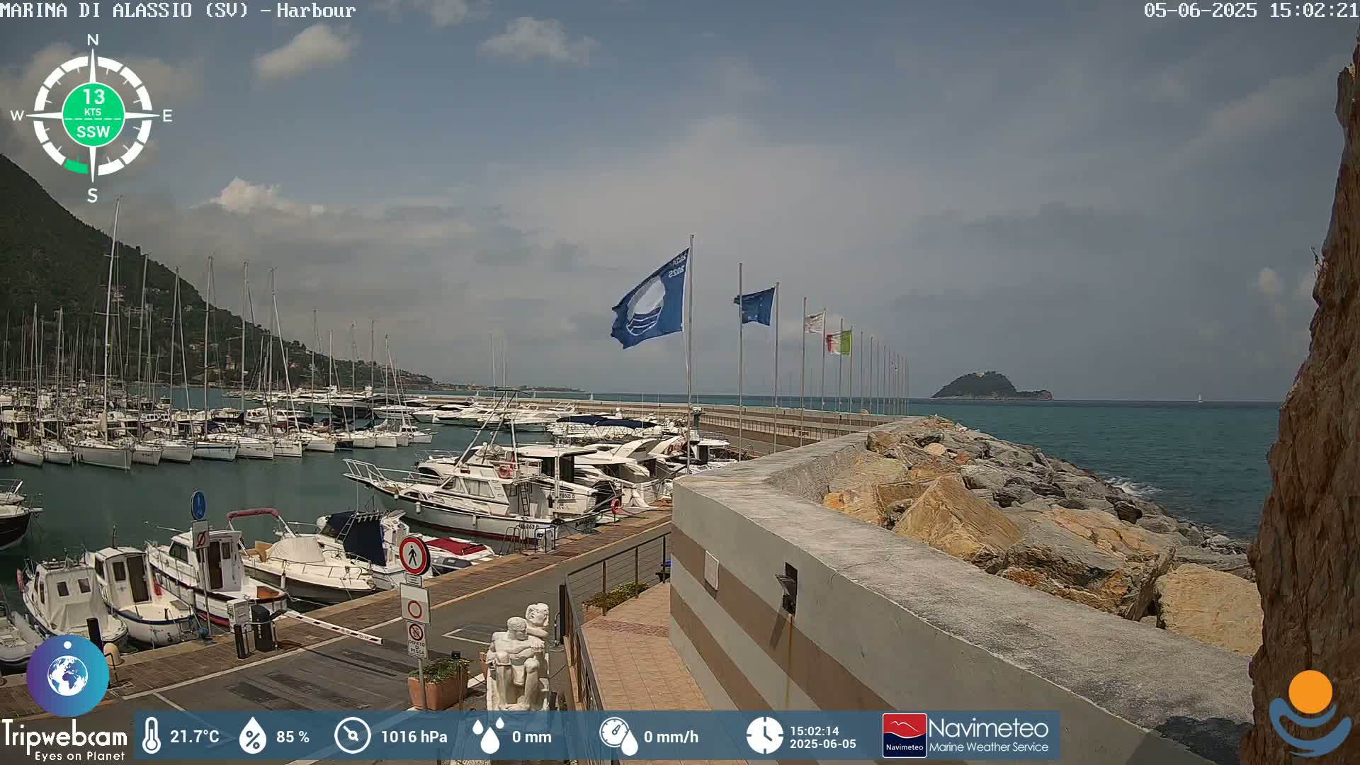 A harbor filled with numerous boats is situated next to a rocky shoreline on a partly cloudy day.