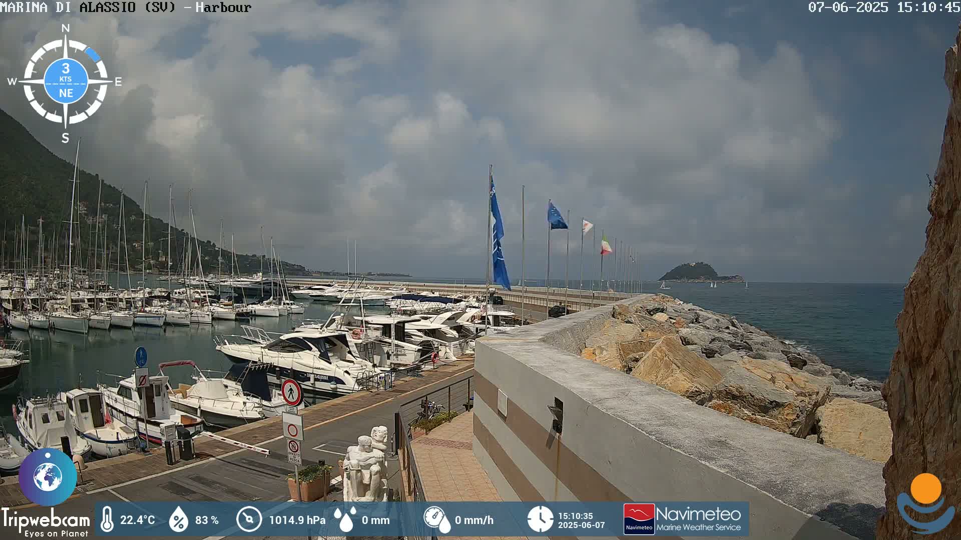 A harbor filled with boats is situated next to a rocky shoreline on a partly cloudy day.